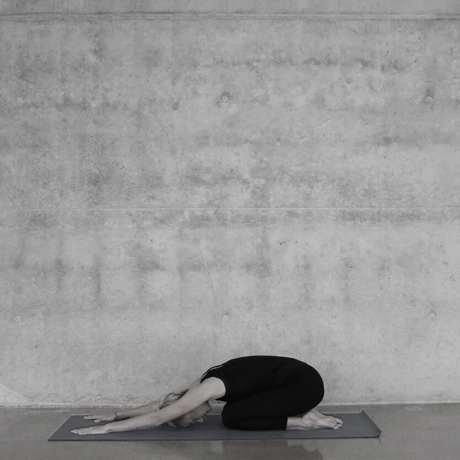 Black-and-white photo of a person resting in a child’s pose on a mat