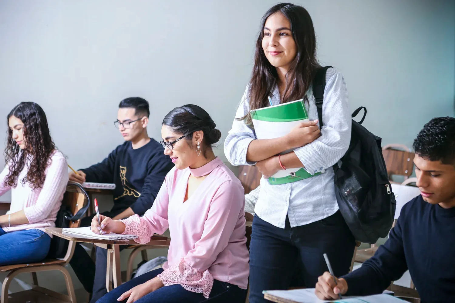 High school students in a classroom, one holding books and smiling