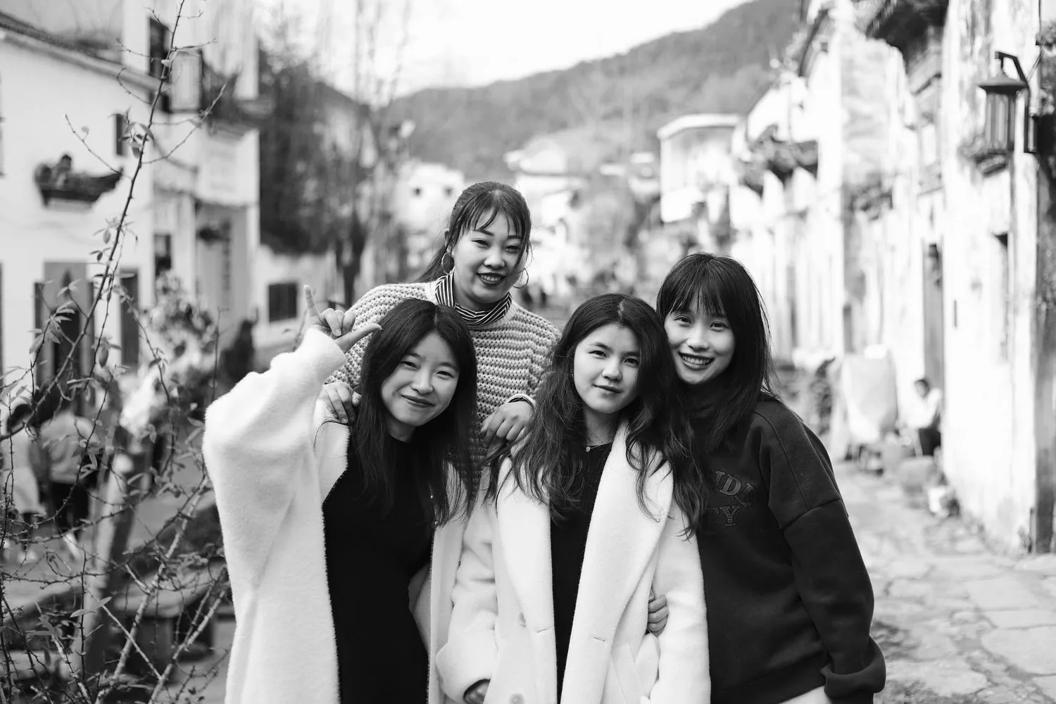 Black-and-white photo of four young East Asian women smiling on a village street