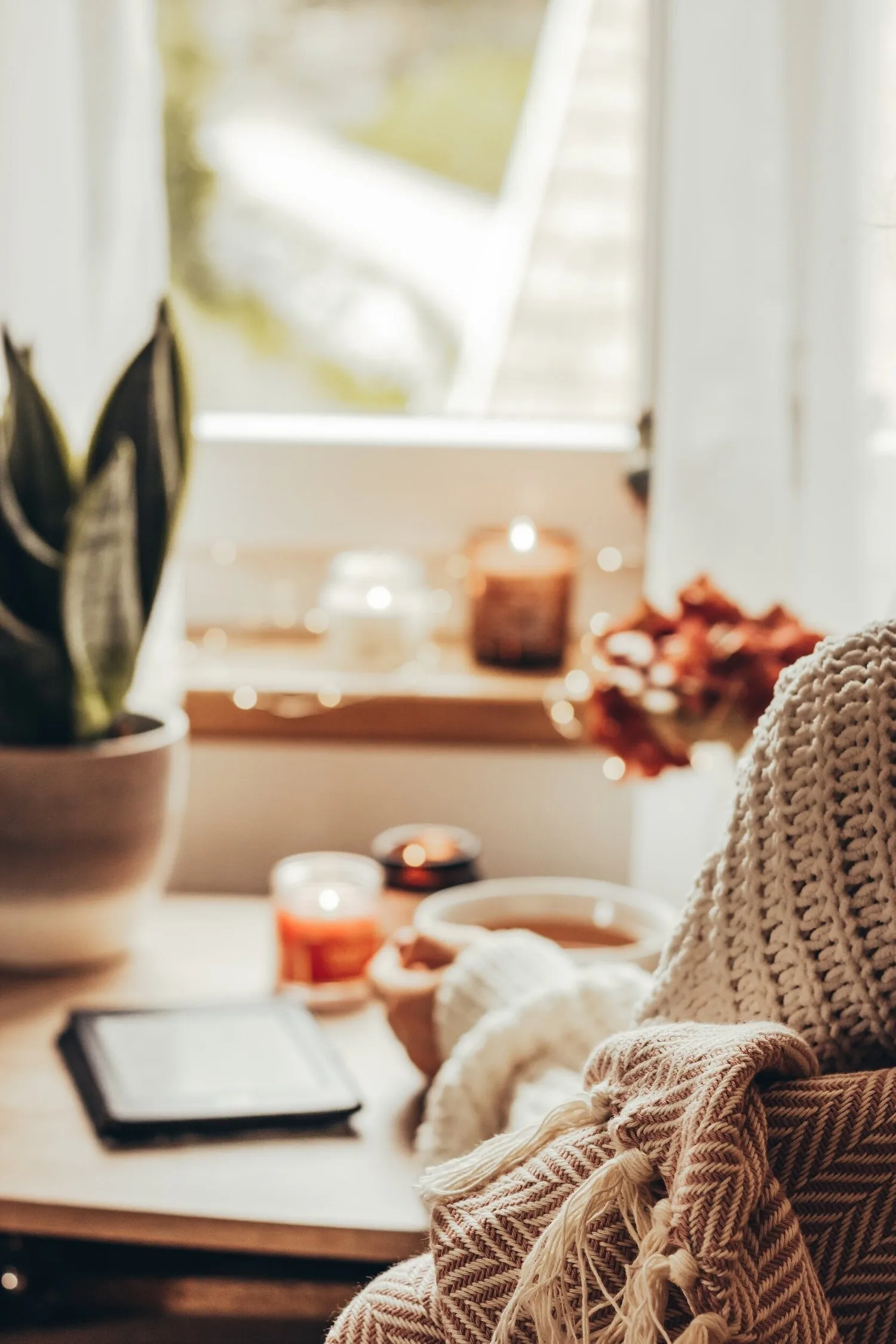 Cozy corner with a tablet, candle, and blanket beside a window