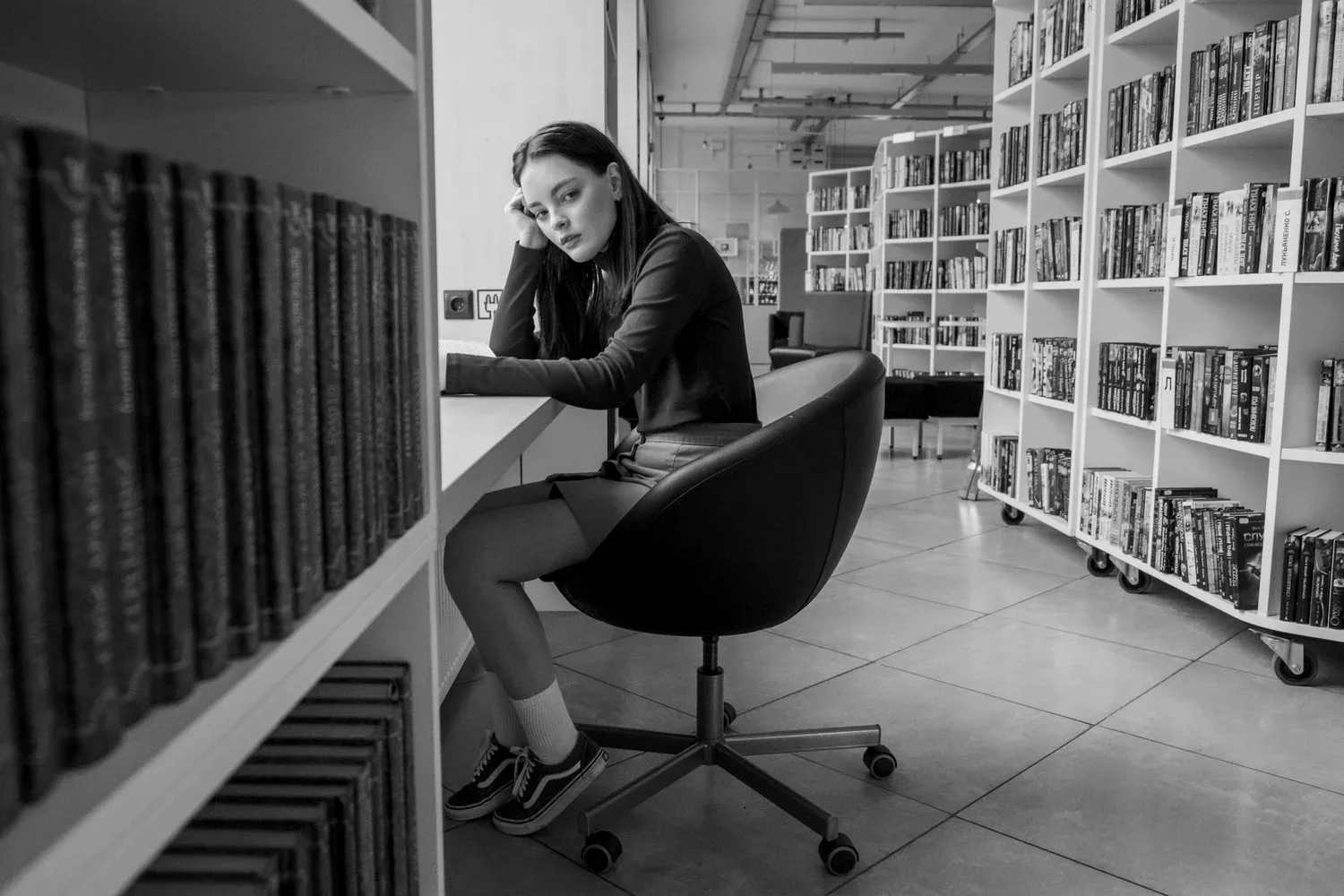 Woman sitting at a desk between tall bookshelves in a library