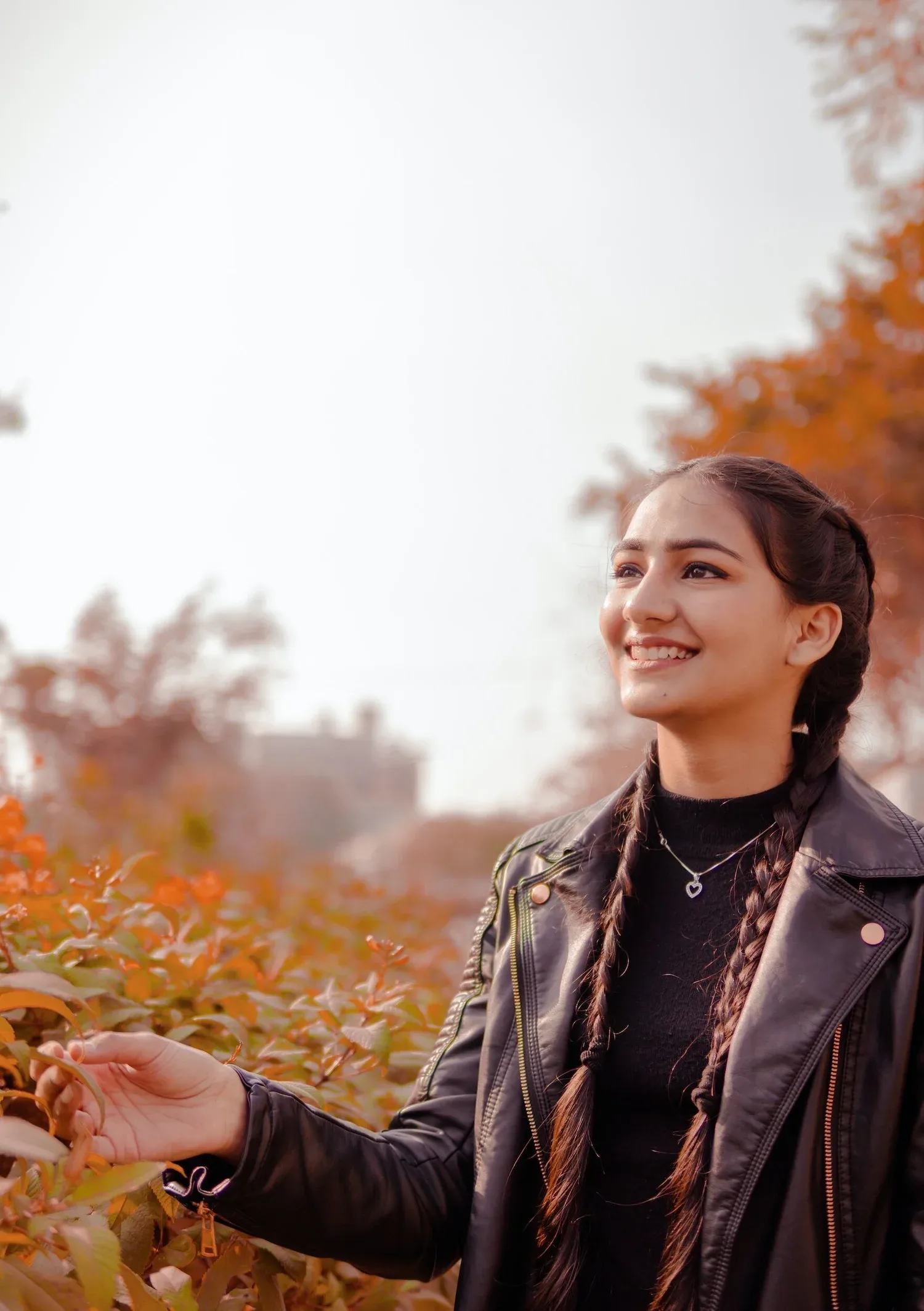 Smiling young woman in a leather jacket outdoors among autumn trees