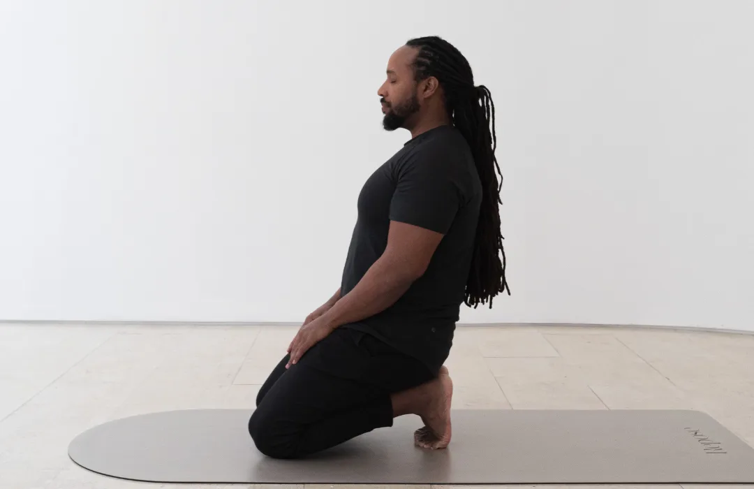 Man kneeling on a mat in profile, sitting upright in a calm posture
