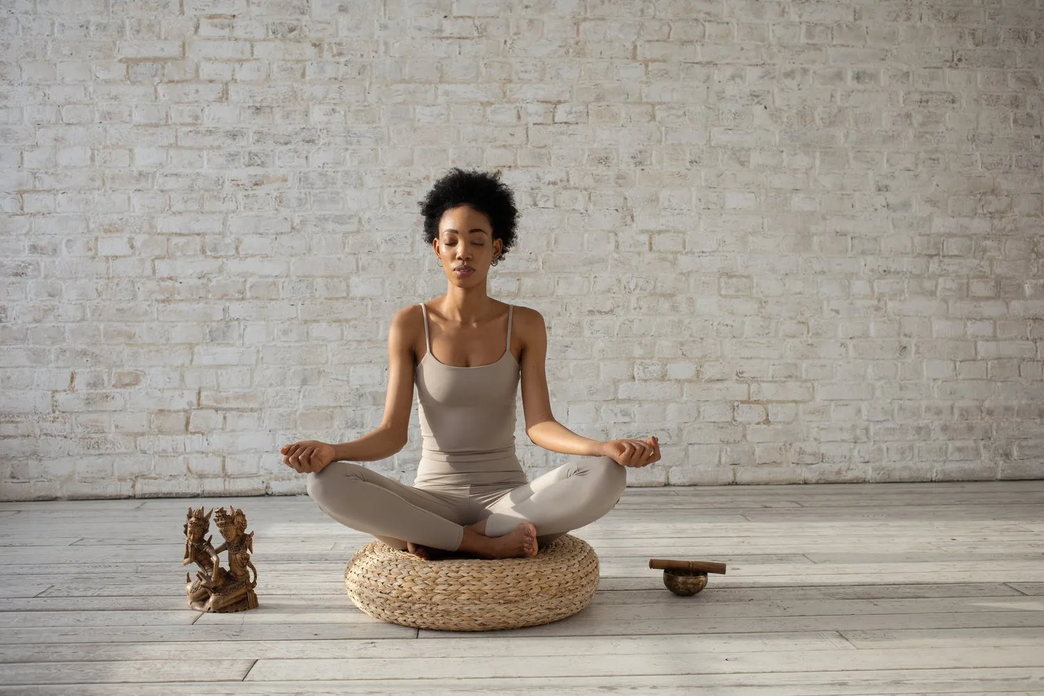 Woman meditating cross-legged on a cushion in a bright brick room