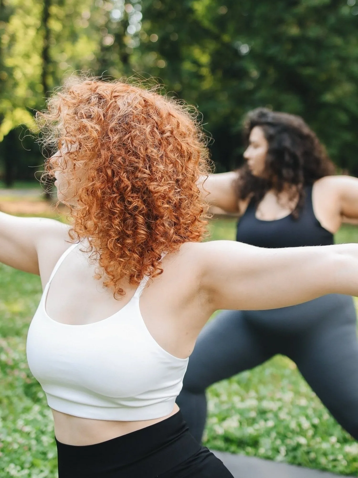 Two women with arms extended in a standing stretch outdoors