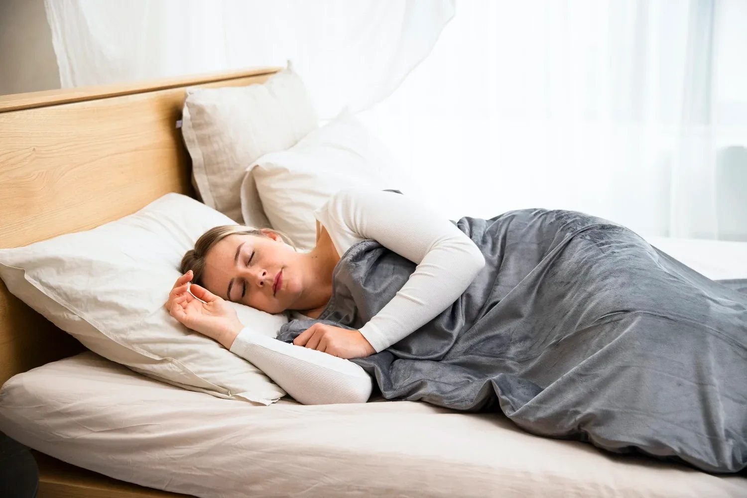 Person asleep in bed under a gray blanket in a bright bedroom