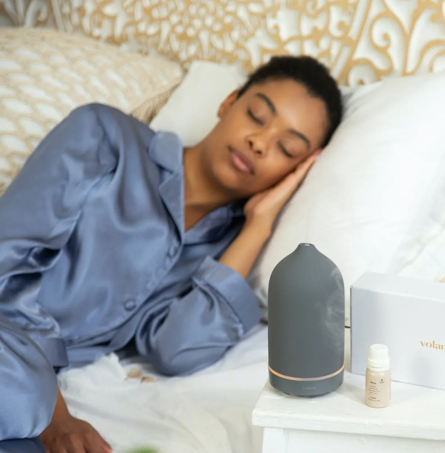 Woman sleeping peacefully in blue pajamas beside a small diffuser