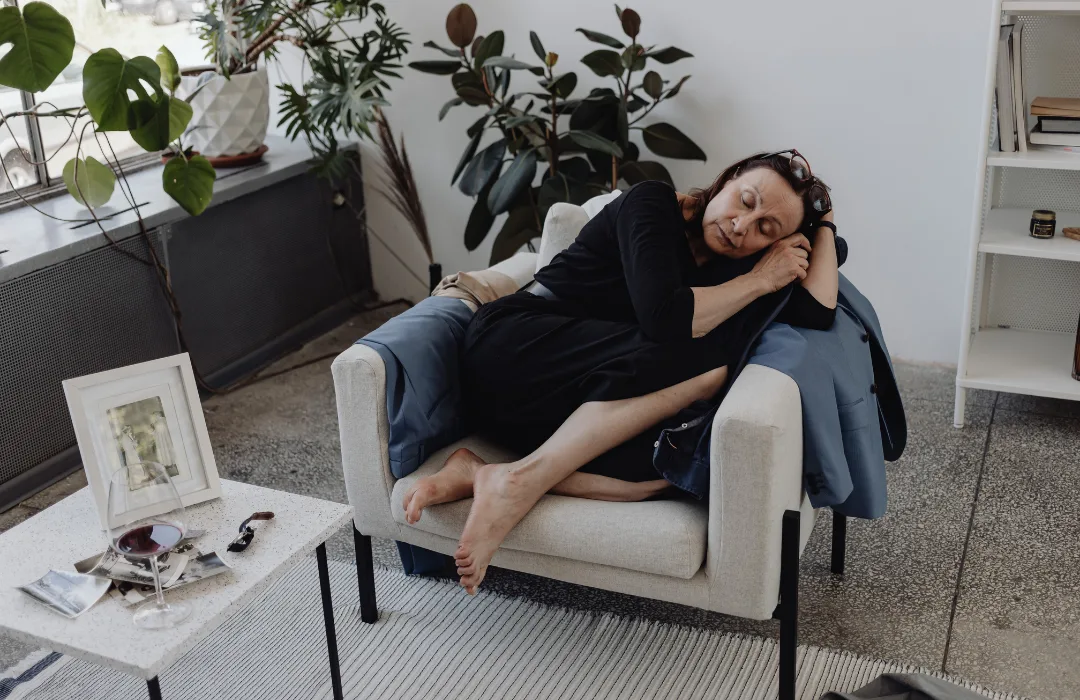 Woman lying back on an armchair with a hand to her forehead, looking exhausted