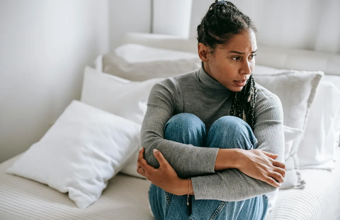 Young woman sitting on a bed hugging her knees, looking withdrawn