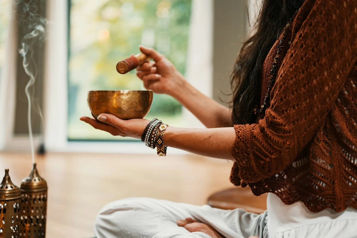 Woman playing a brass singing bowl with a mallet in a sunlit room