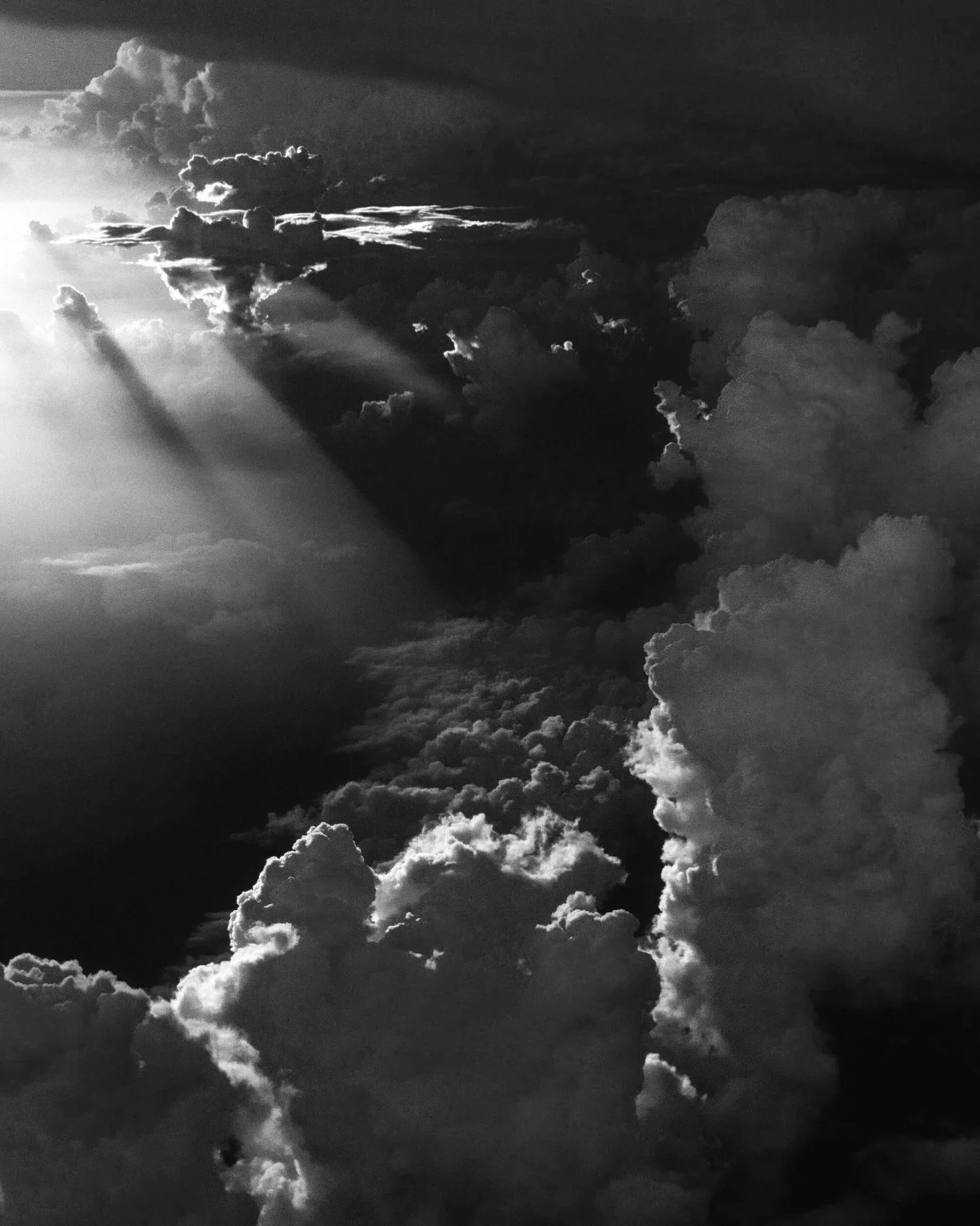 Black-and-white photo of billowing clouds lit by rays of sun