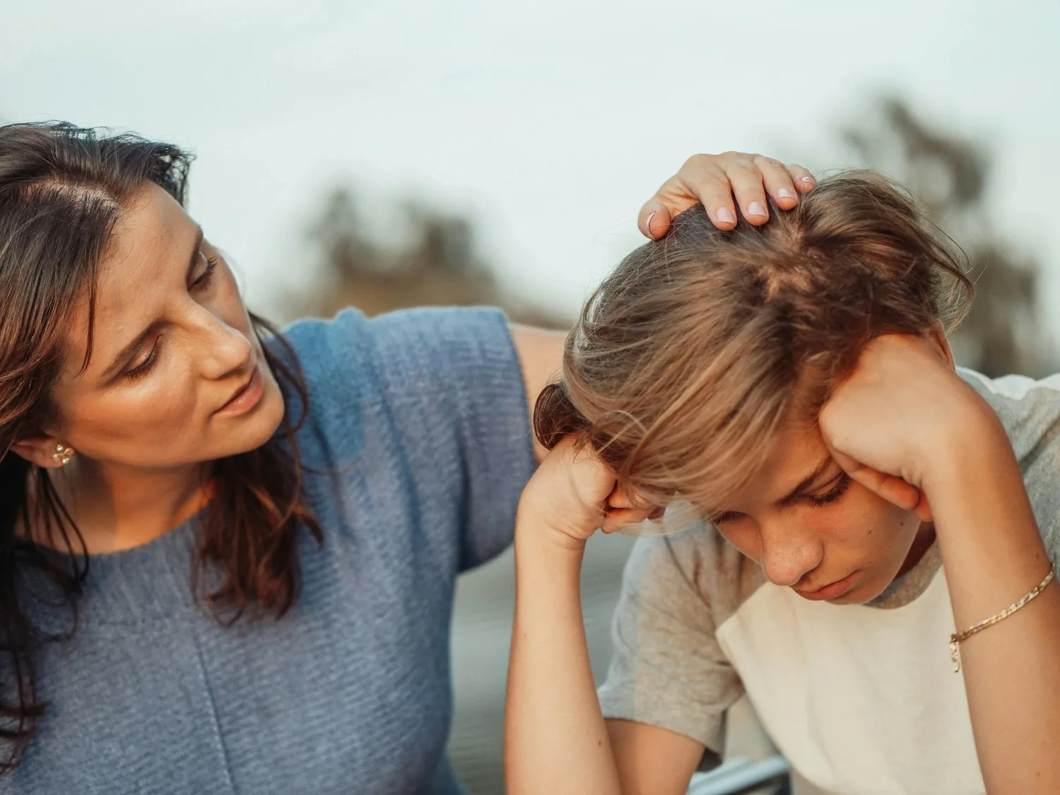 Mother gently touching her teenage son’s head as he sits with his head in his hands