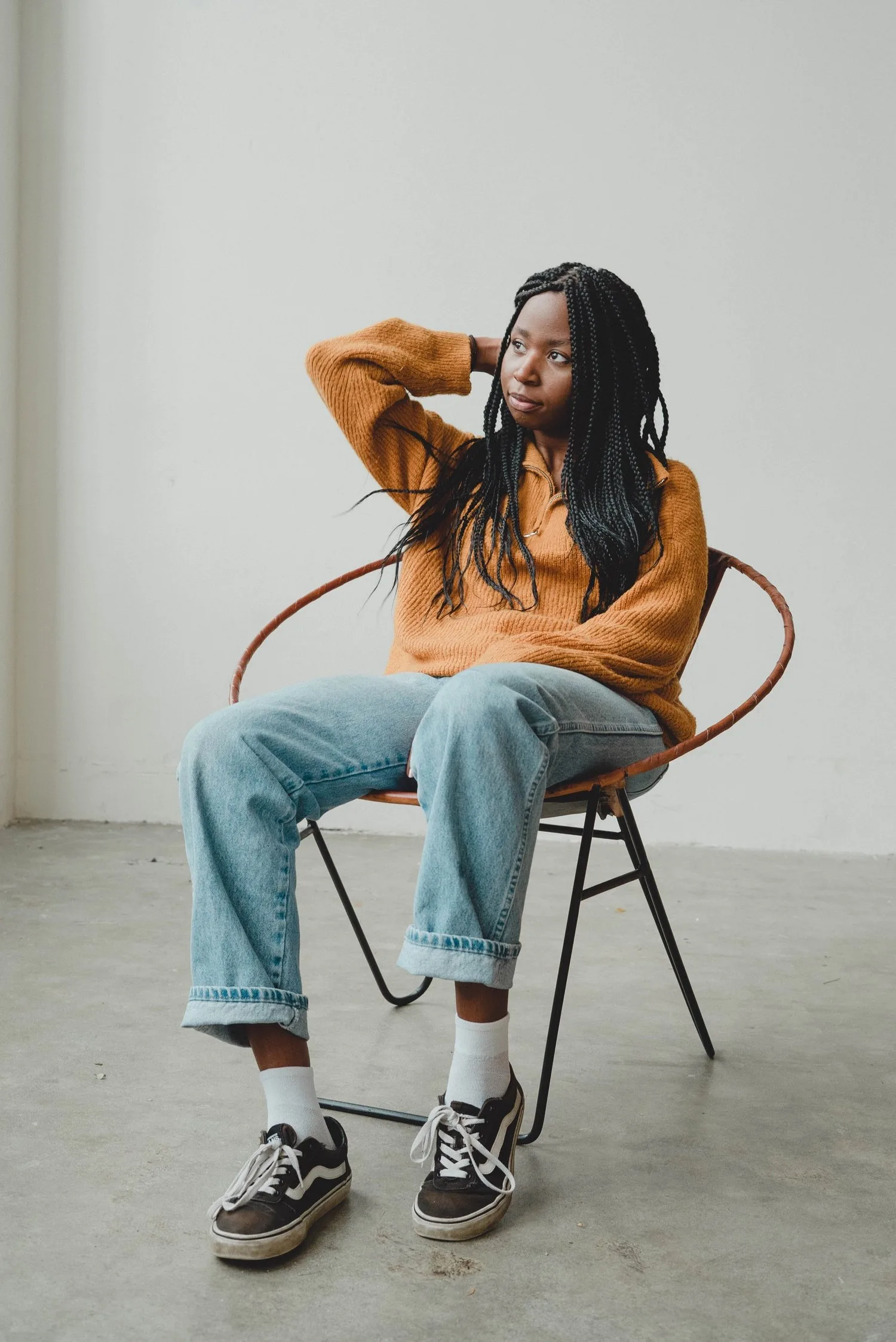 Teenager in an orange hoodie sitting on a chair, looking down