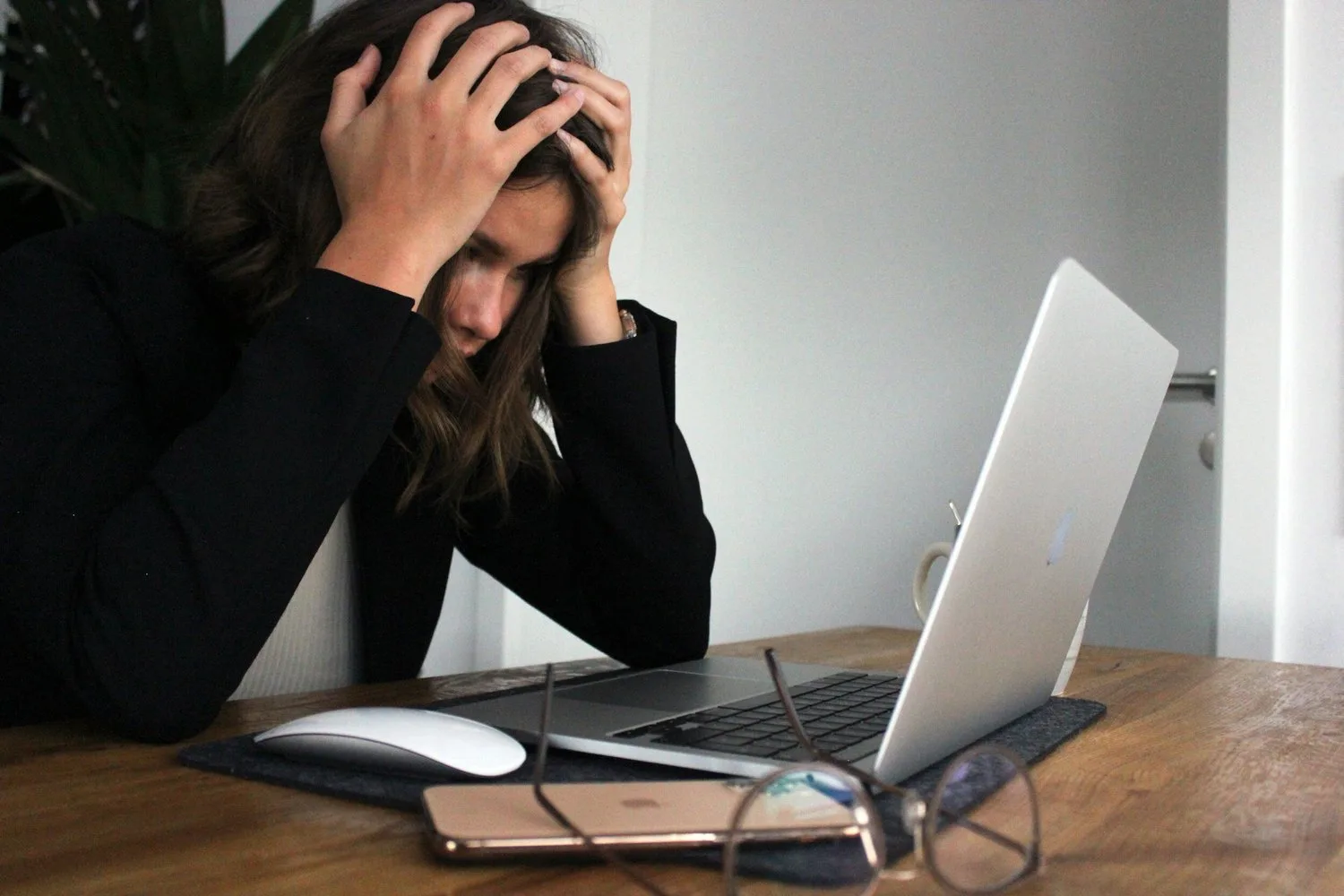 Woman at a desk with her head in her hands in front of a laptop