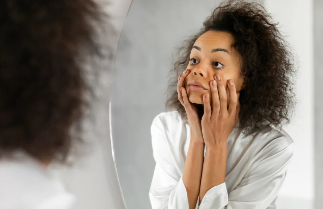 Woman with curly hair holding her face in her hands with a surprised, anxious look