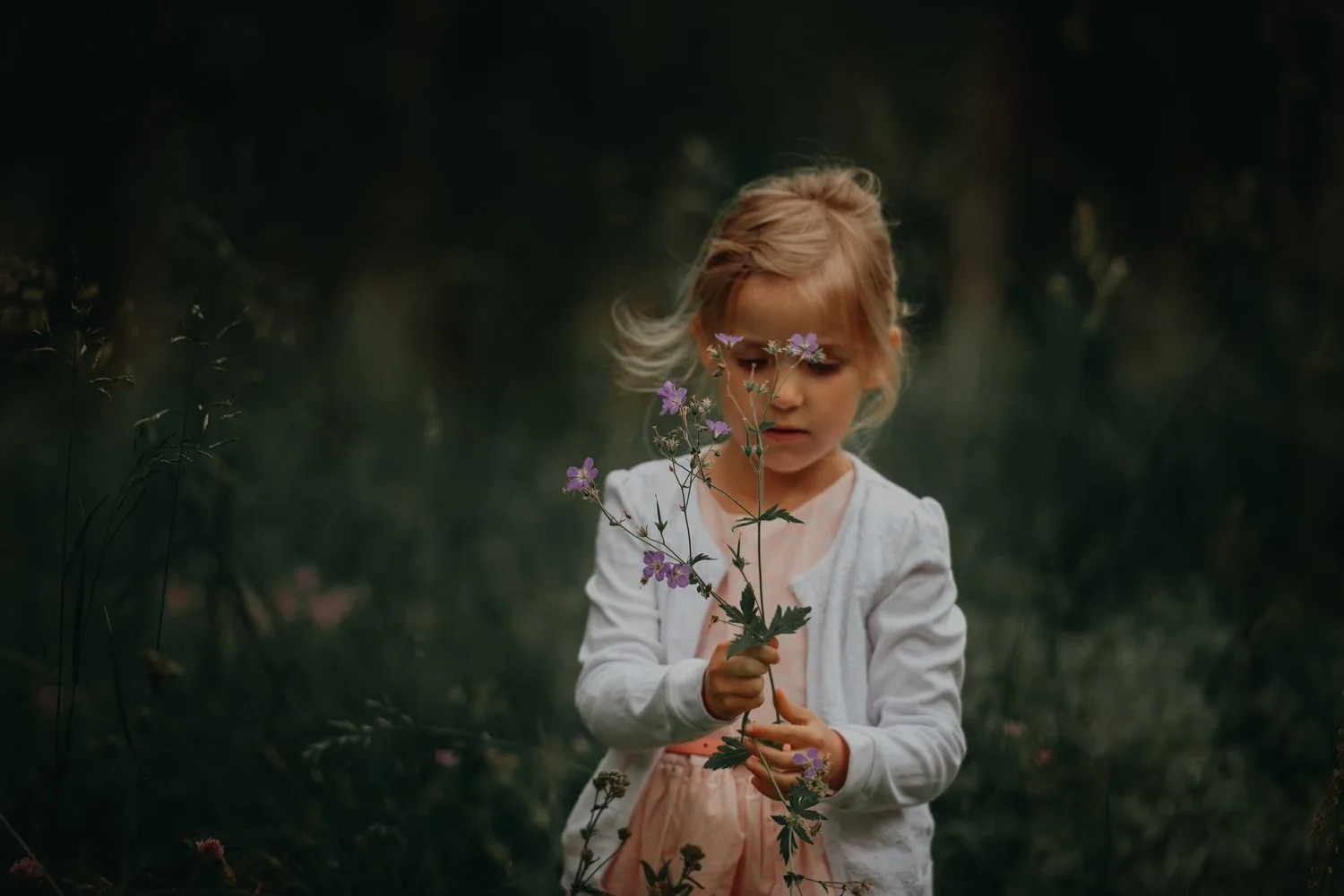 Young child in a dark forest looking down at something held in her hands