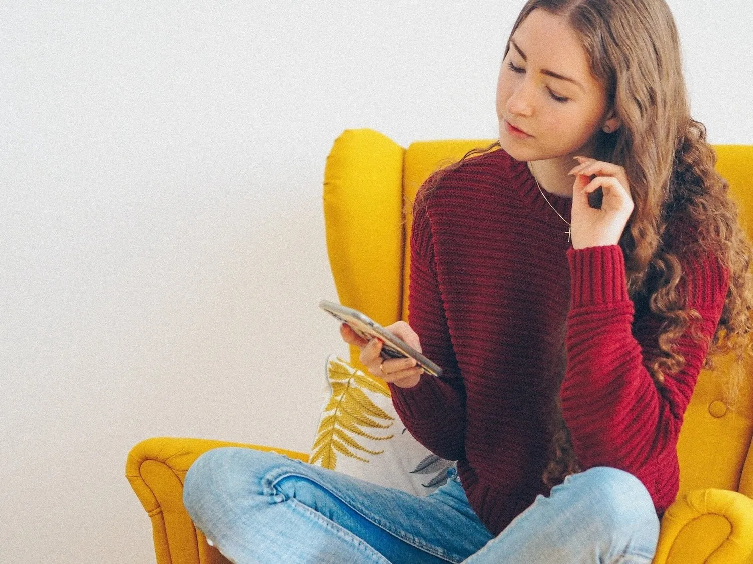 Woman in a red sweater sitting in a yellow chair looking at her phone