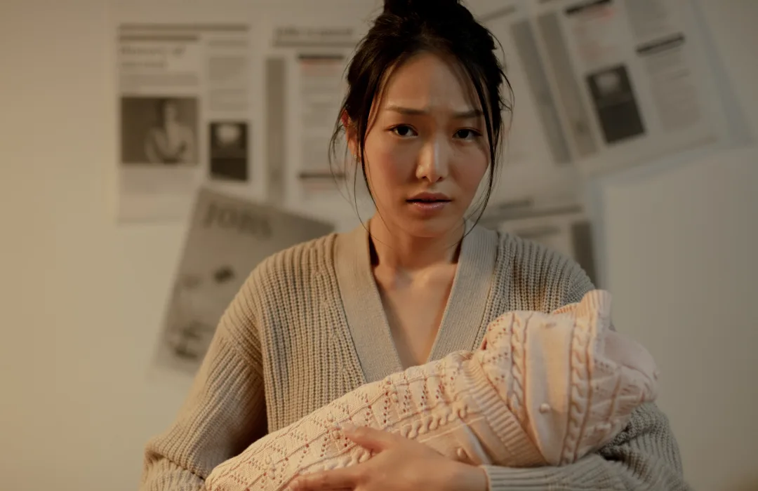 Woman holding a newborn wrapped in a knit blanket, looking tired