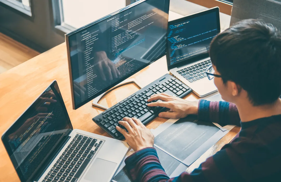 Person coding at a desk with multiple monitors and a laptop