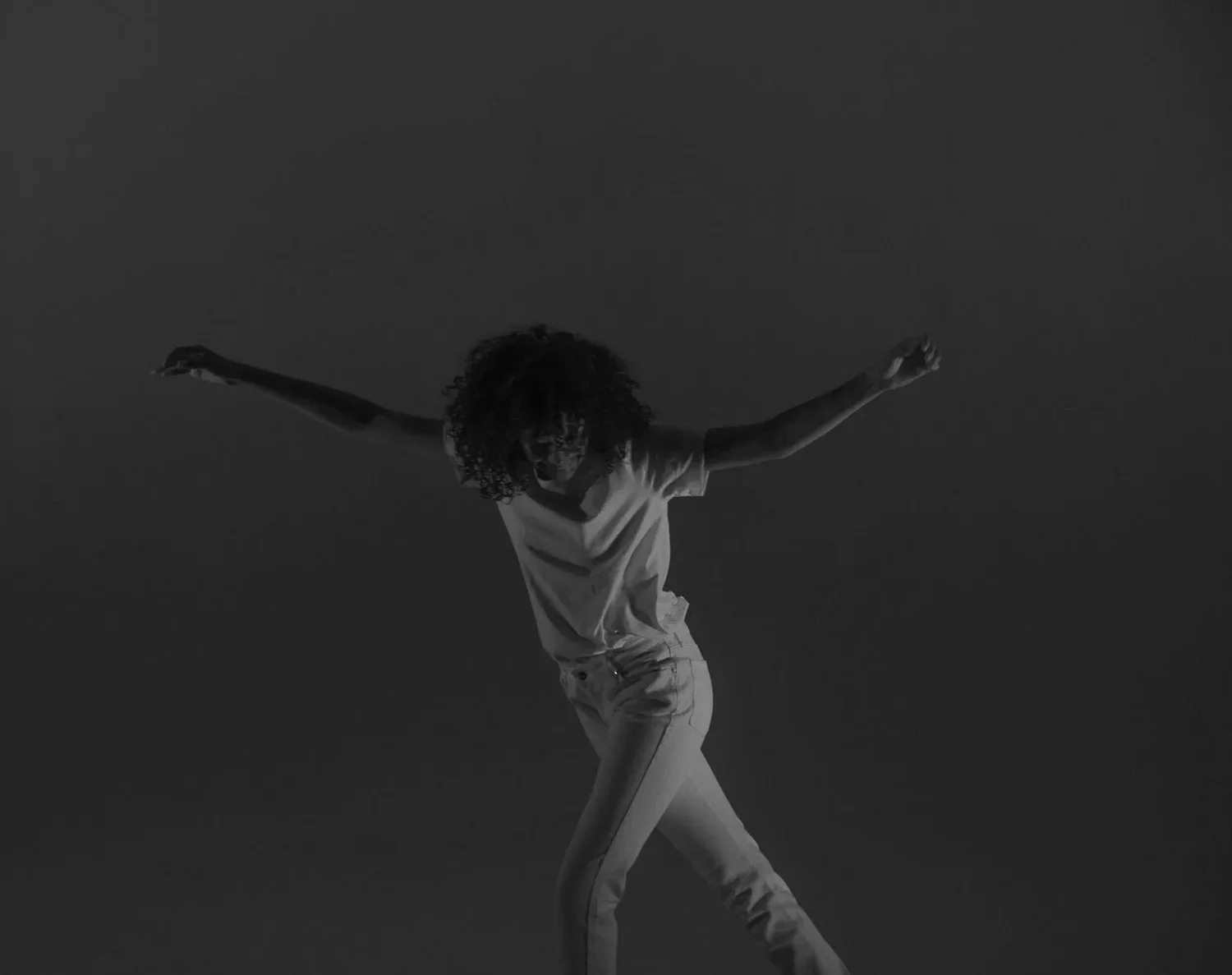 Black-and-white photo of a person dancing with arms outstretched in a dark space