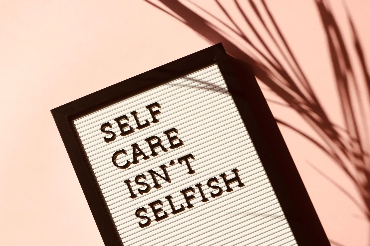 Framed sign reading SELF CARE ISN’T SELFISH beside a palm frond