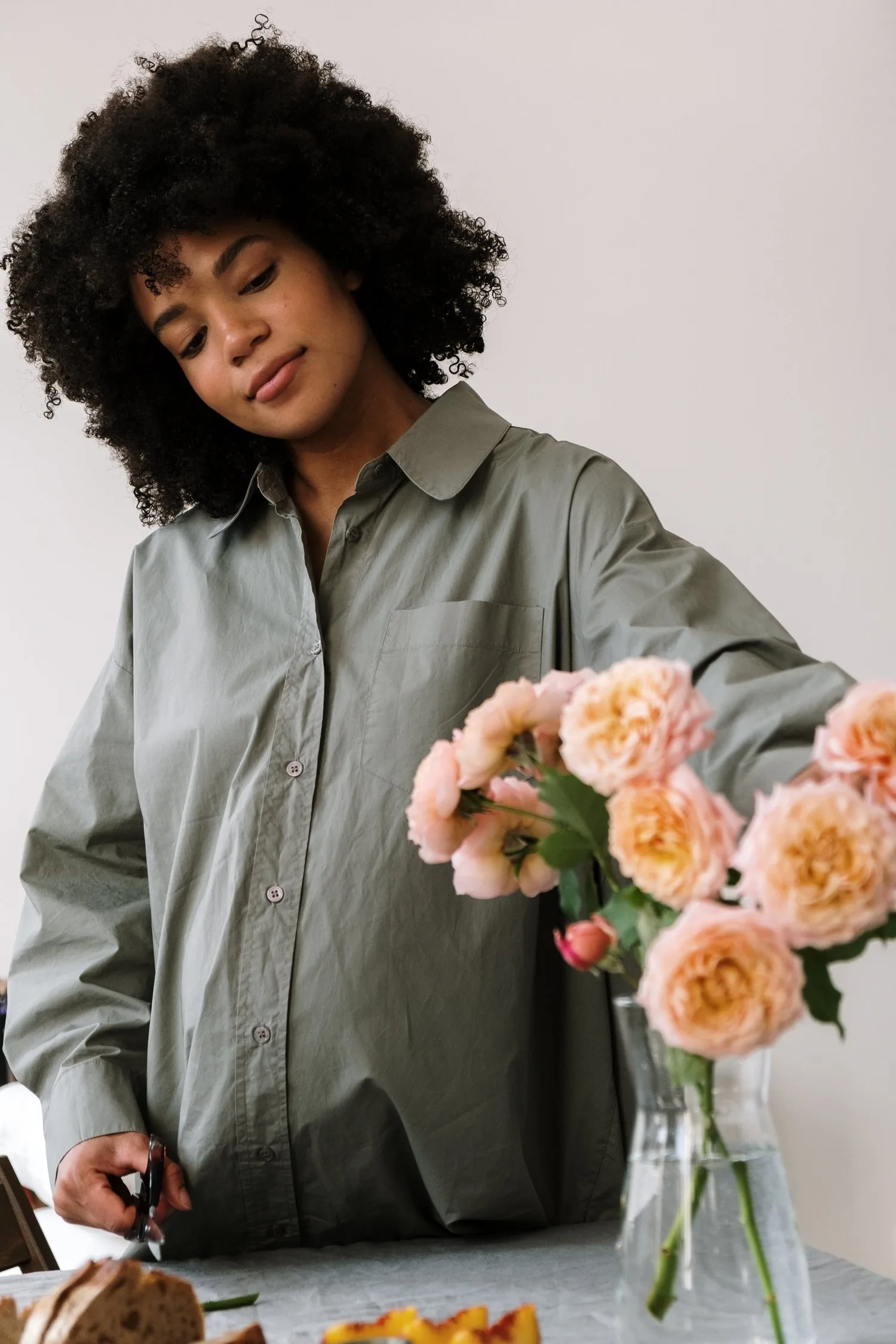 Woman arranging a vase of peach roses on a table