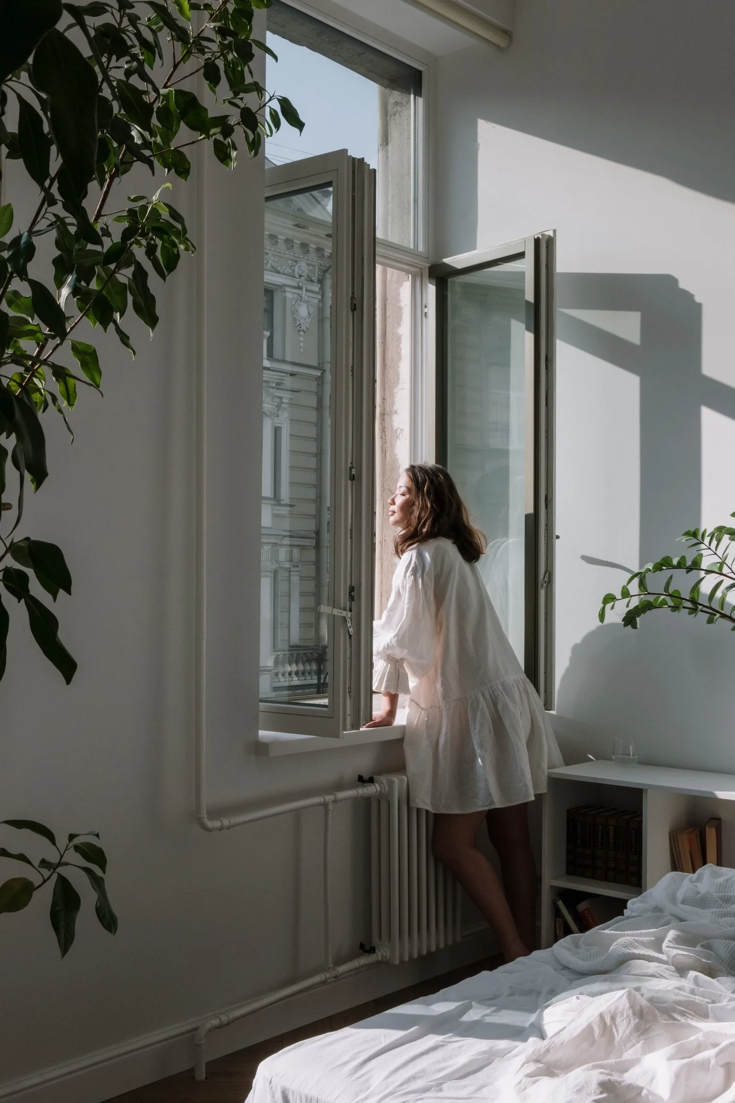 Person standing at an open window in a bright, quiet room