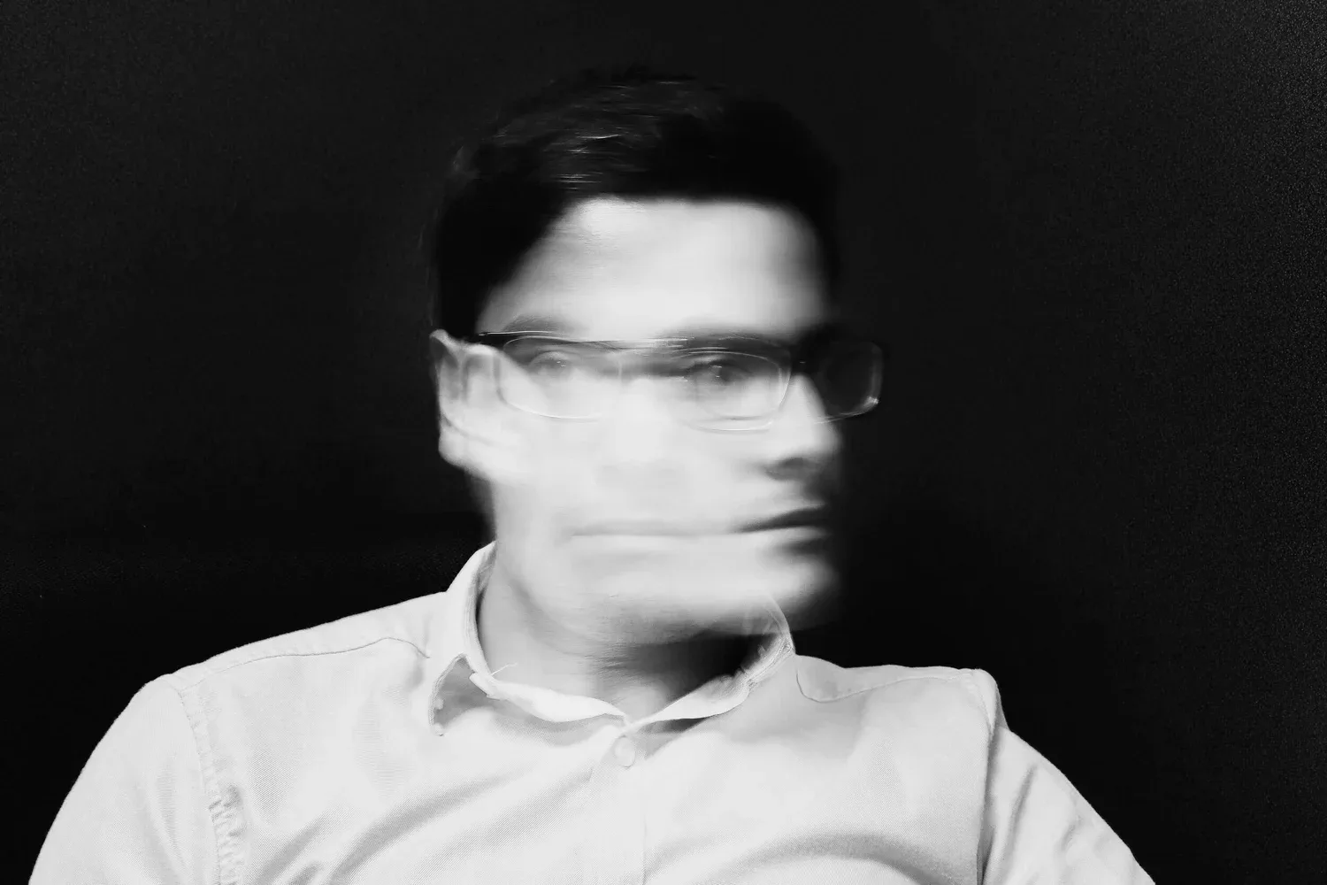 Black-and-white photo of a man in glasses with his face blurred in motion