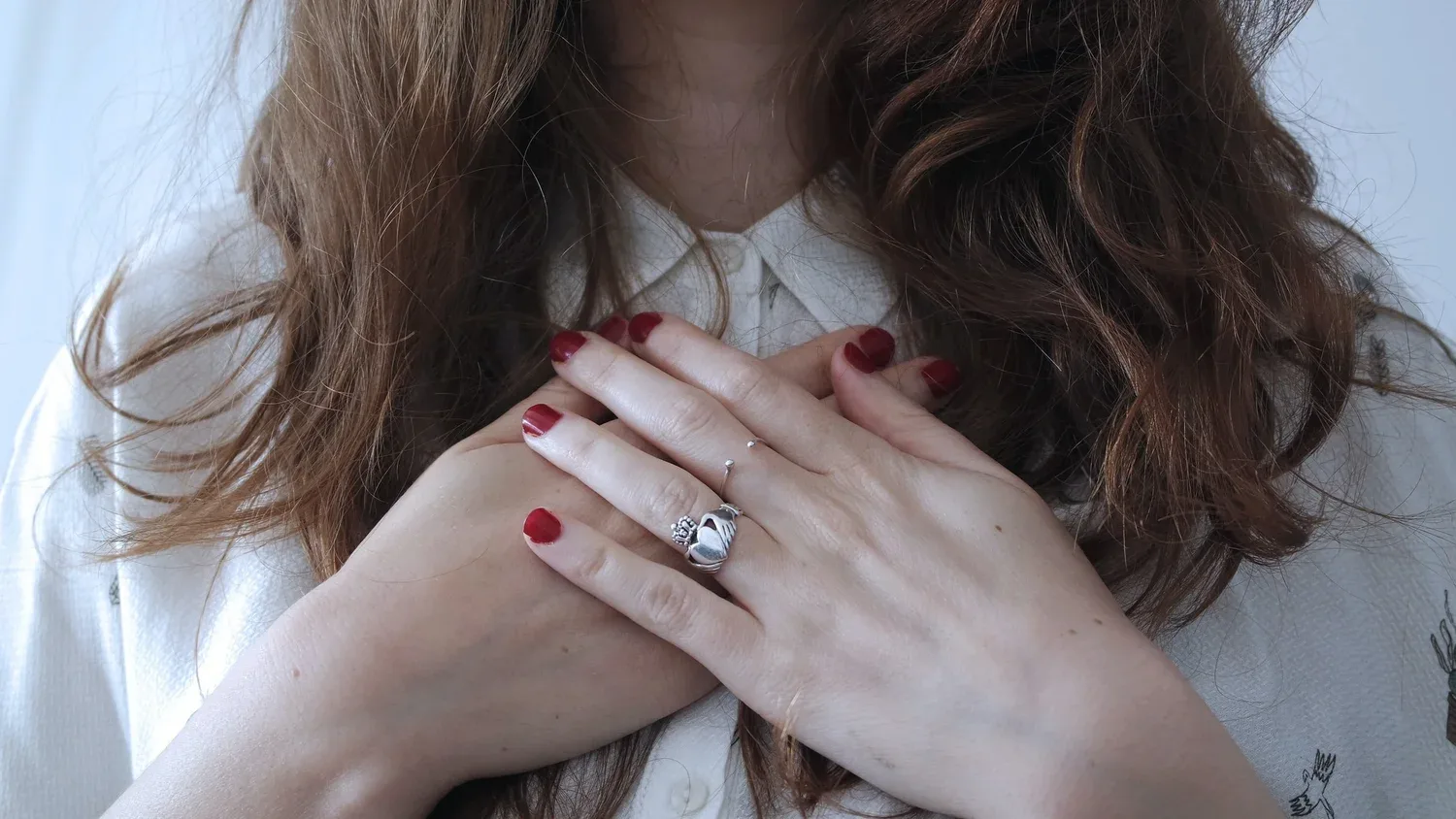 Close-up of hands with red nails resting over the heart