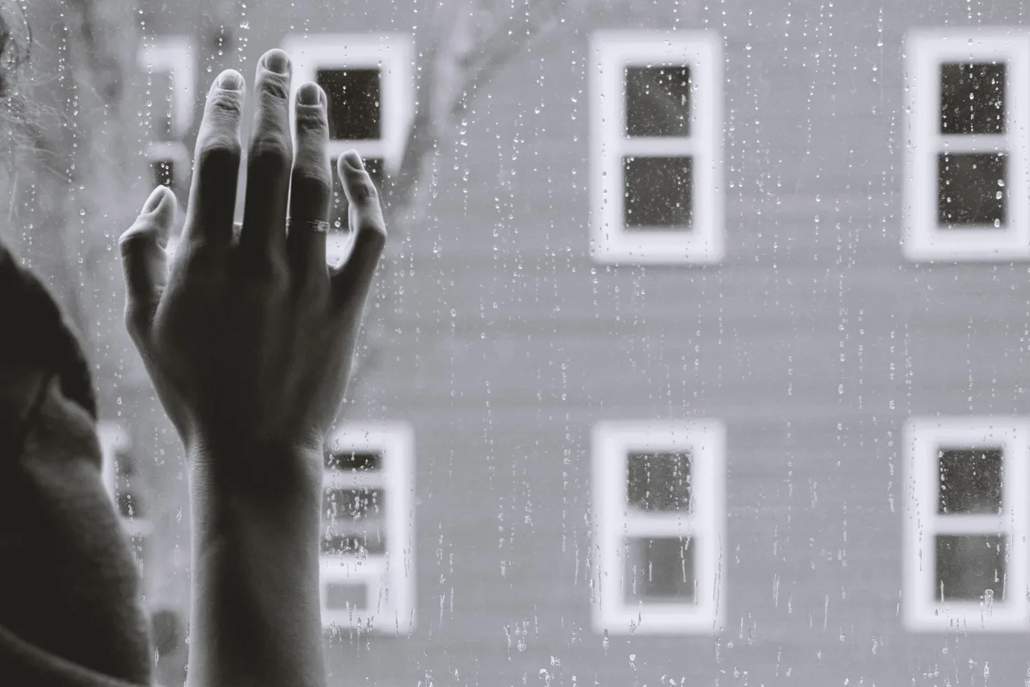 Black-and-white photo of a hand pressed against a window