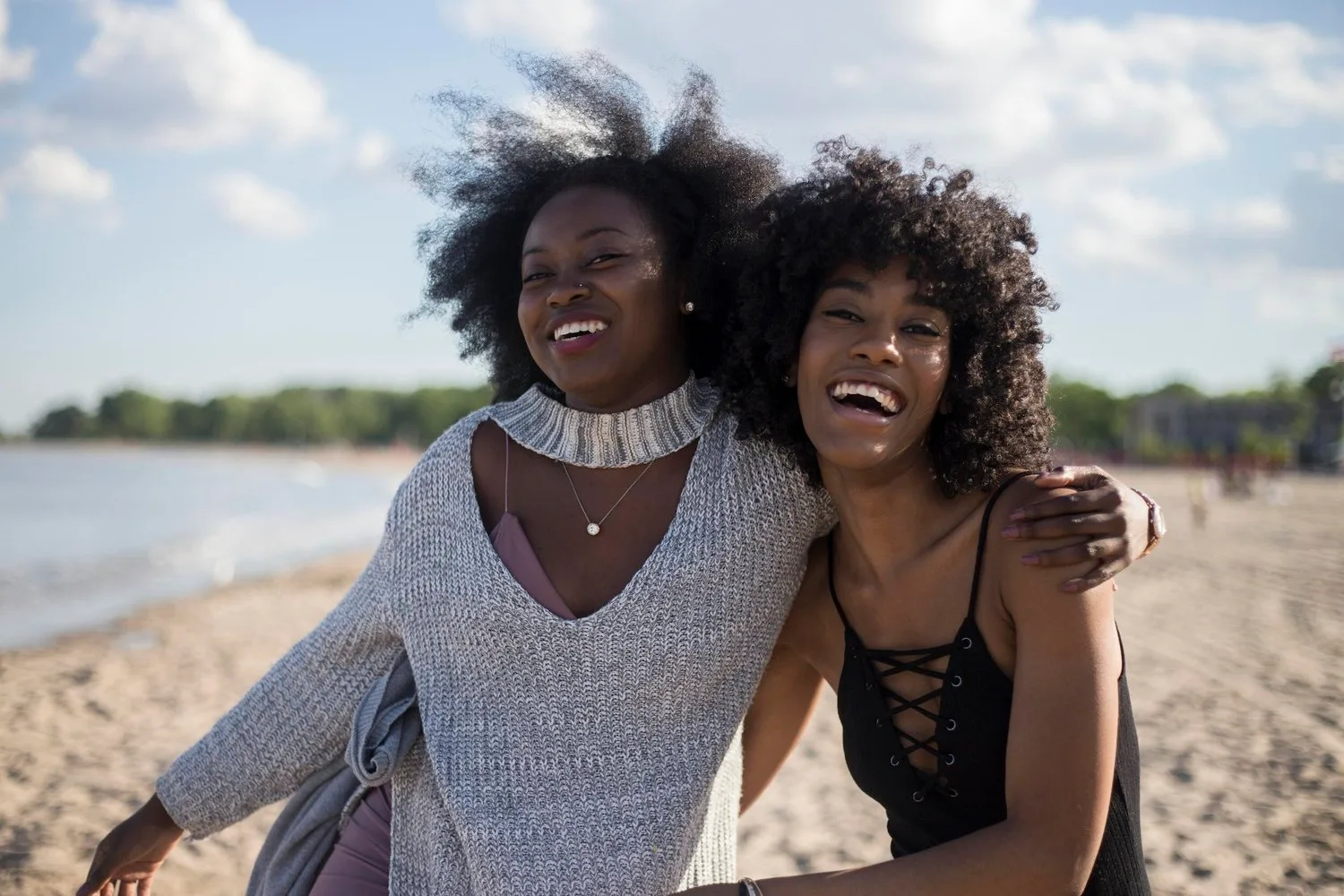 Two women with curly hair laughing and embracing on a beach