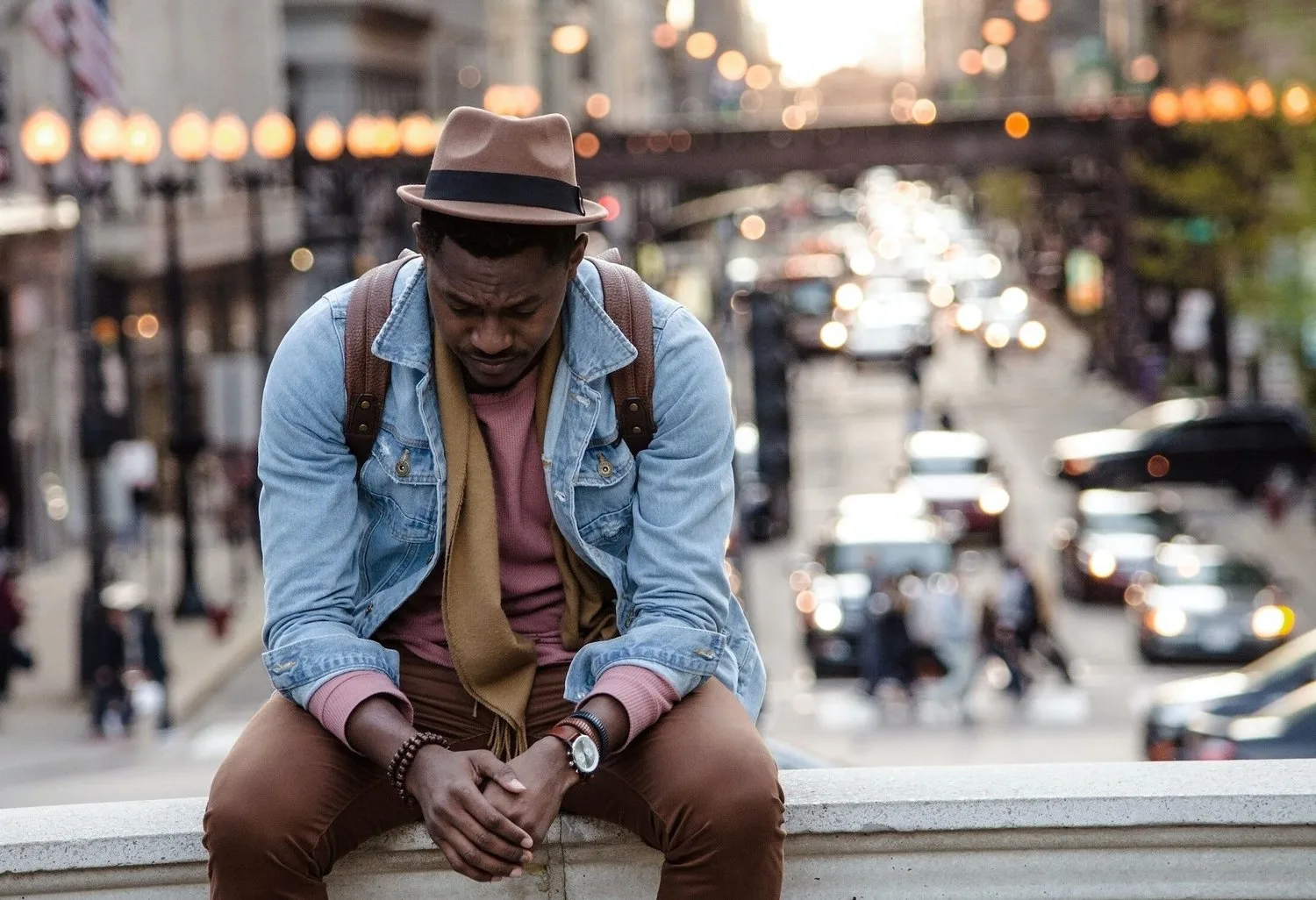 Man in a denim jacket sitting on a city ledge above busy traffic