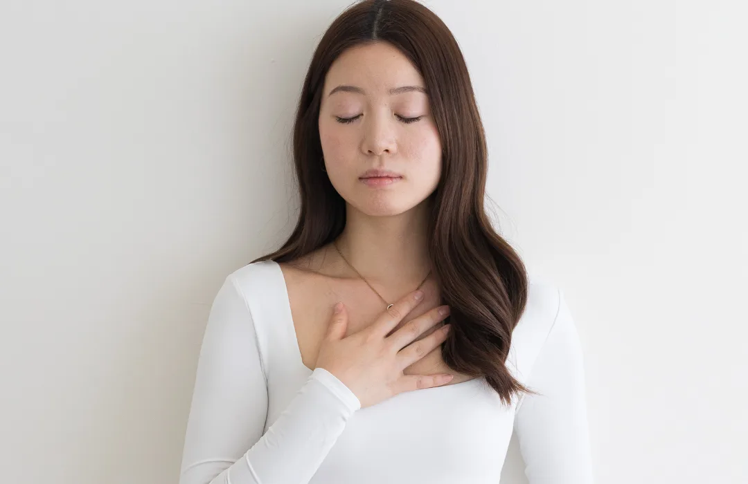 Woman in a white top with eyes closed and one hand resting on her chest