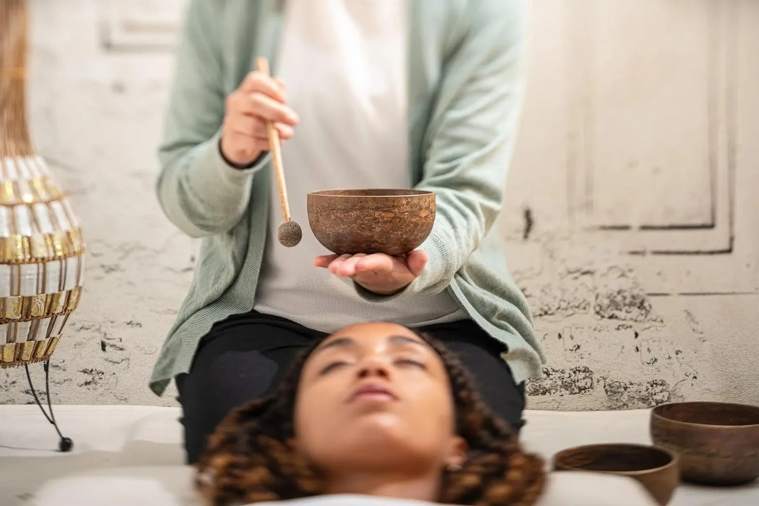Person lying down with eyes closed while a practitioner holds a singing bowl above them