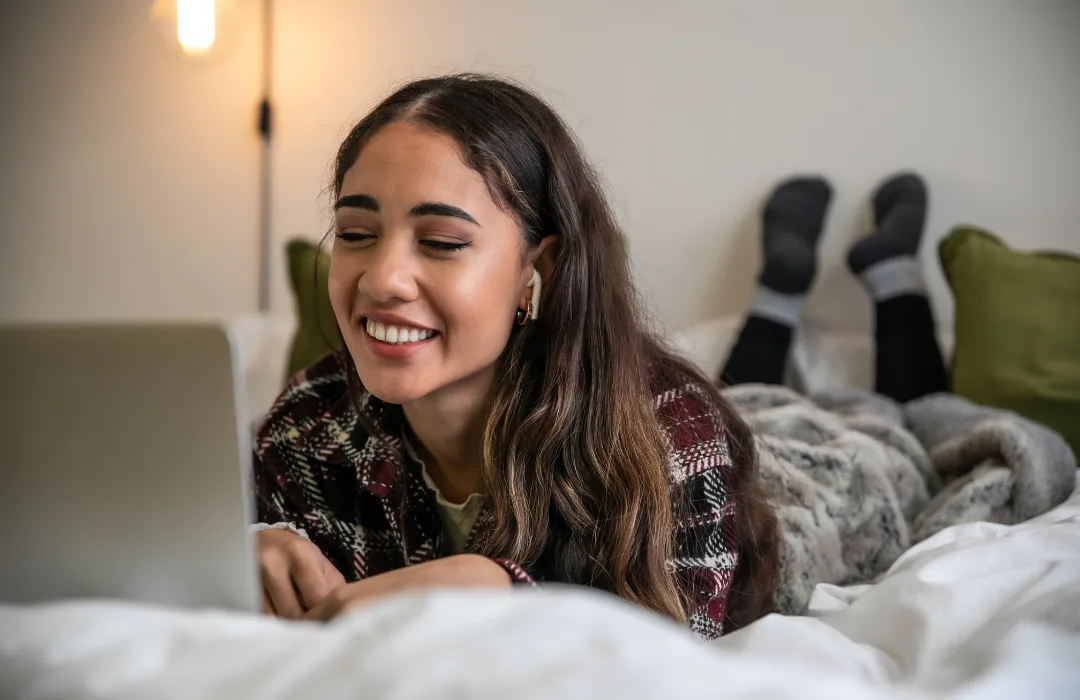 Smiling young woman lying on a bed looking at a laptop