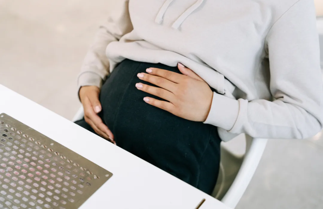 Pregnant person in a light sweater resting both hands on their belly
