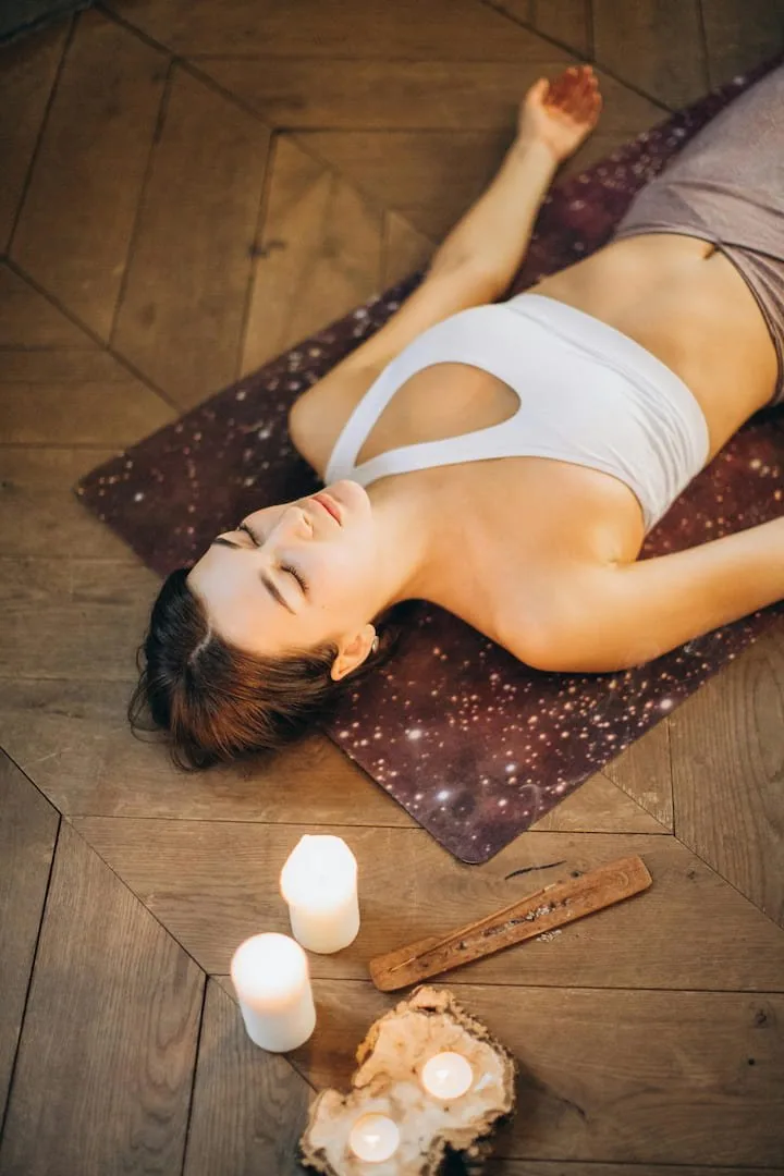 Woman lying on a rug surrounded by candles with eyes closed, resting