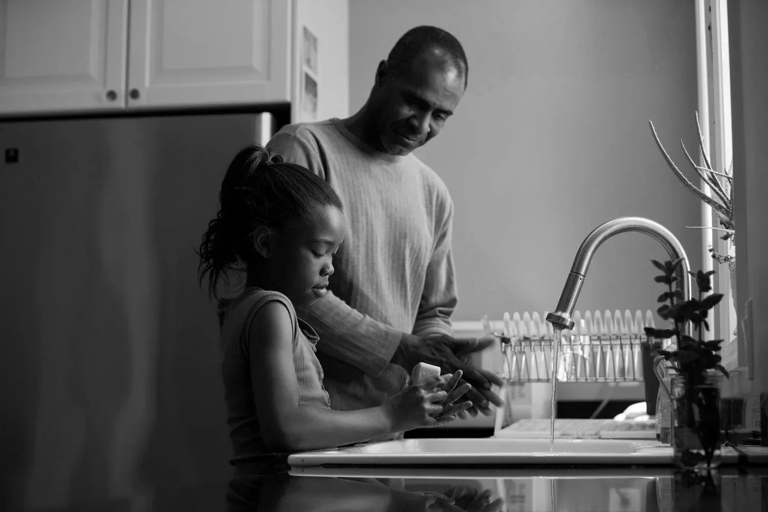 Father and child washing dishes together at a kitchen sink