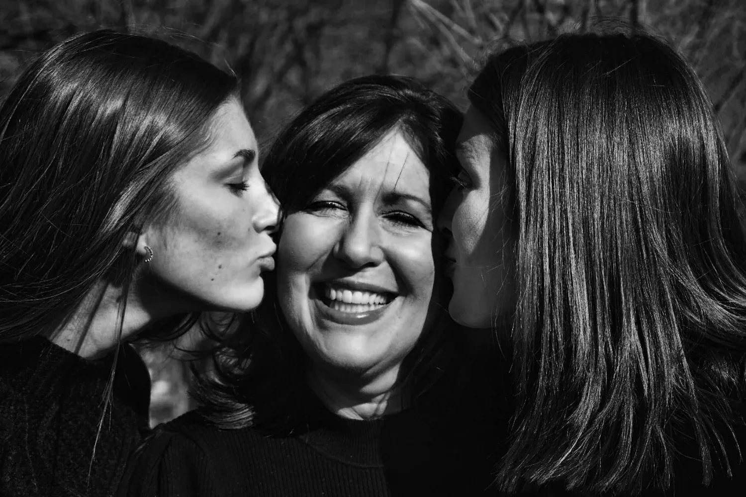 Black-and-white photo of three women smiling and kissing each other’s cheeks