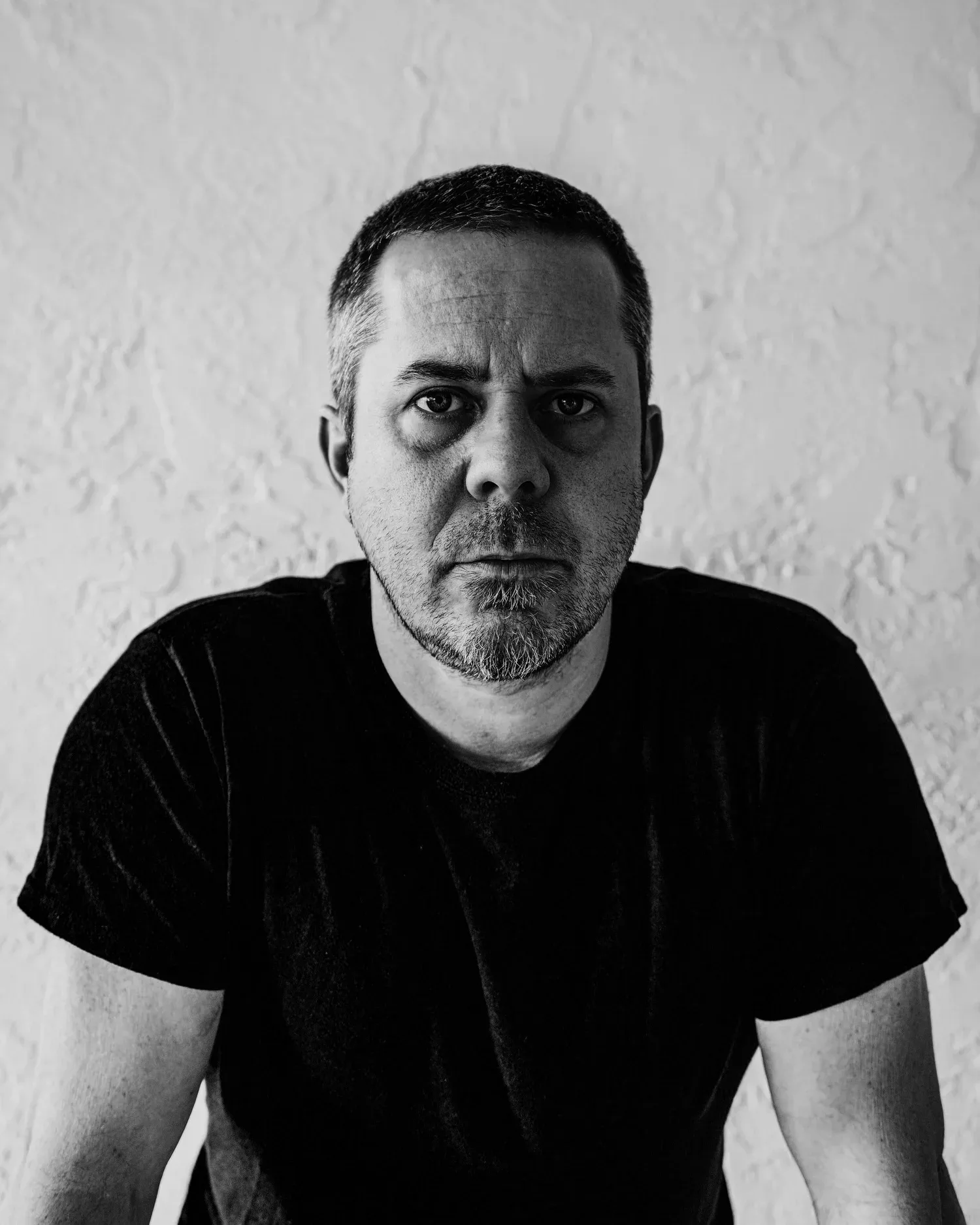 Black-and-white portrait of a man in a dark T-shirt with a serious expression