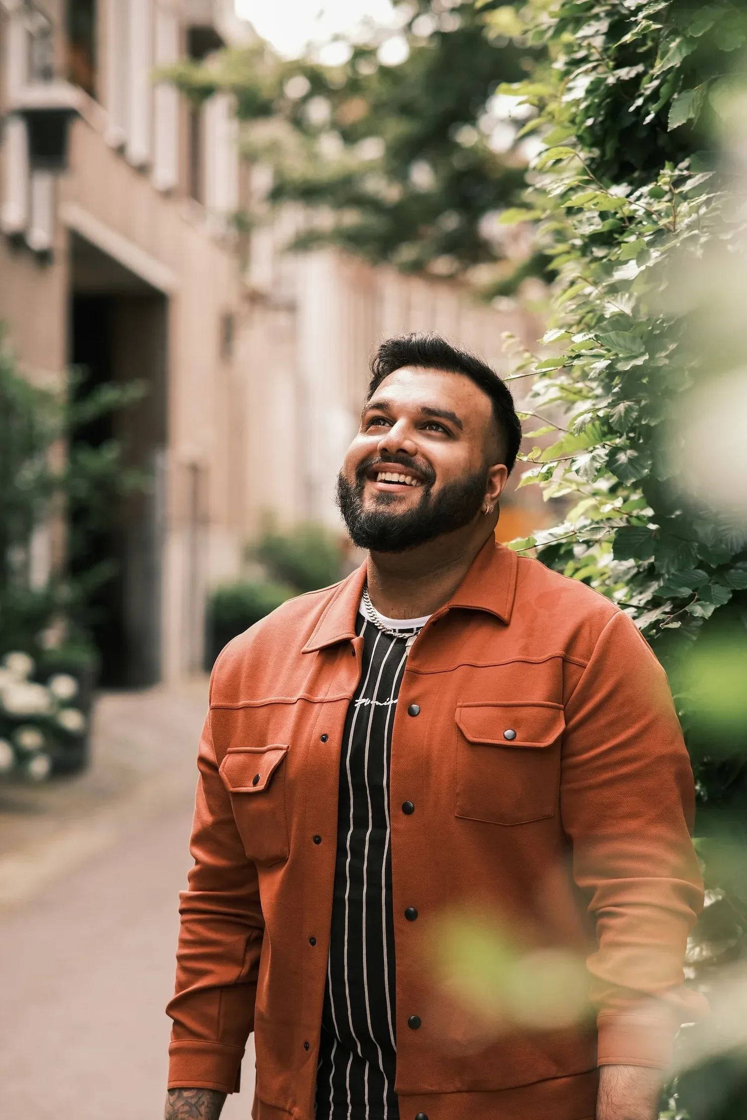 Smiling man in a rust-colored jacket standing on a leafy street
