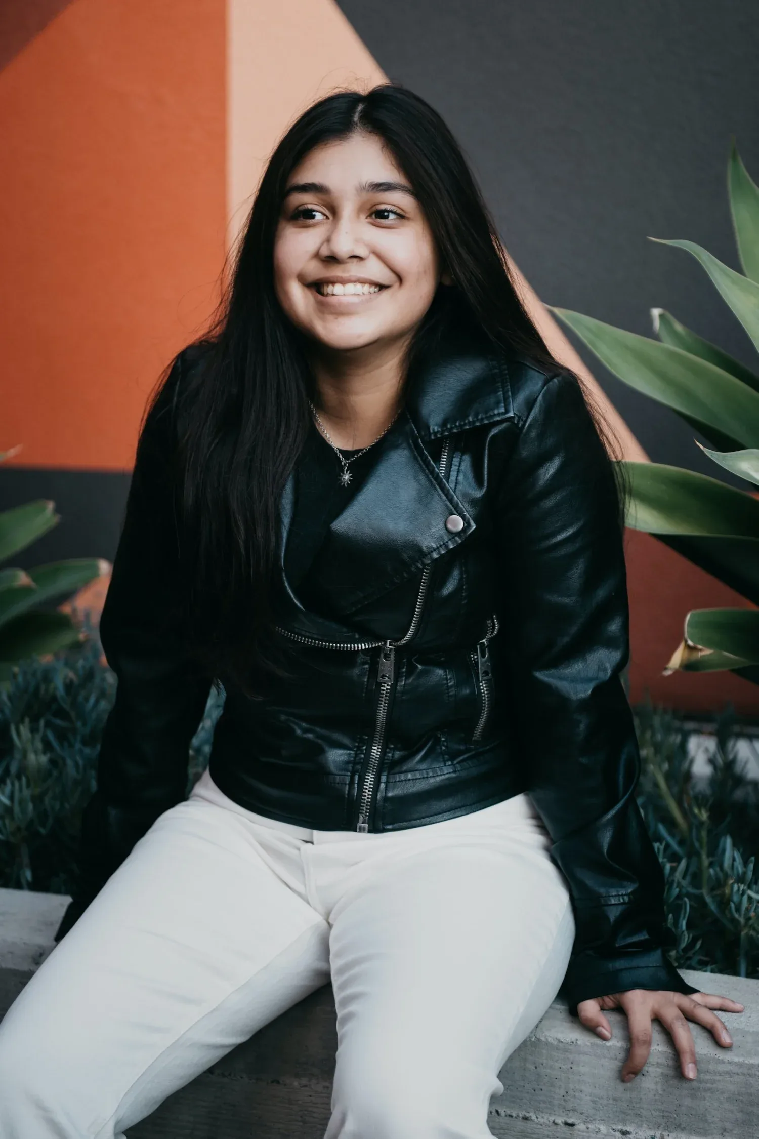 Smiling young woman in a leather jacket seated outdoors