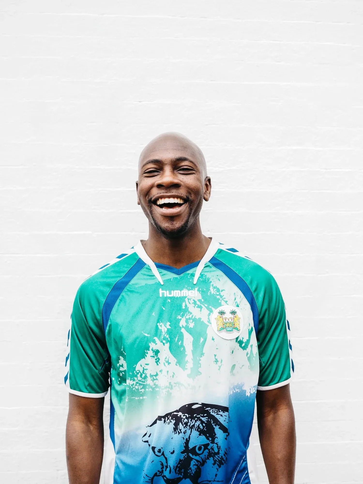 Smiling man in a green patterned jersey against a white wall