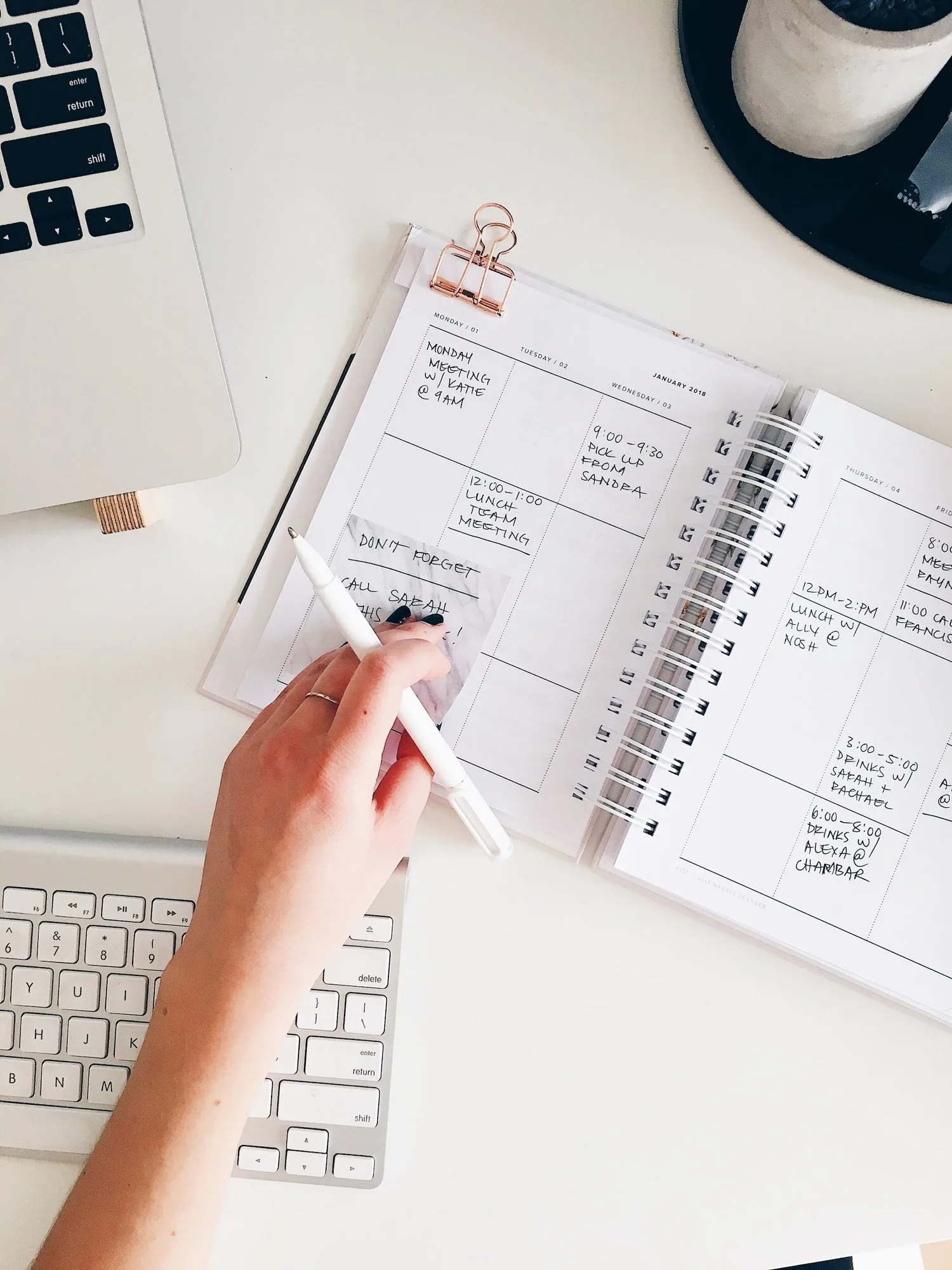 Hand holding a pen over an open planner next to a keyboard
