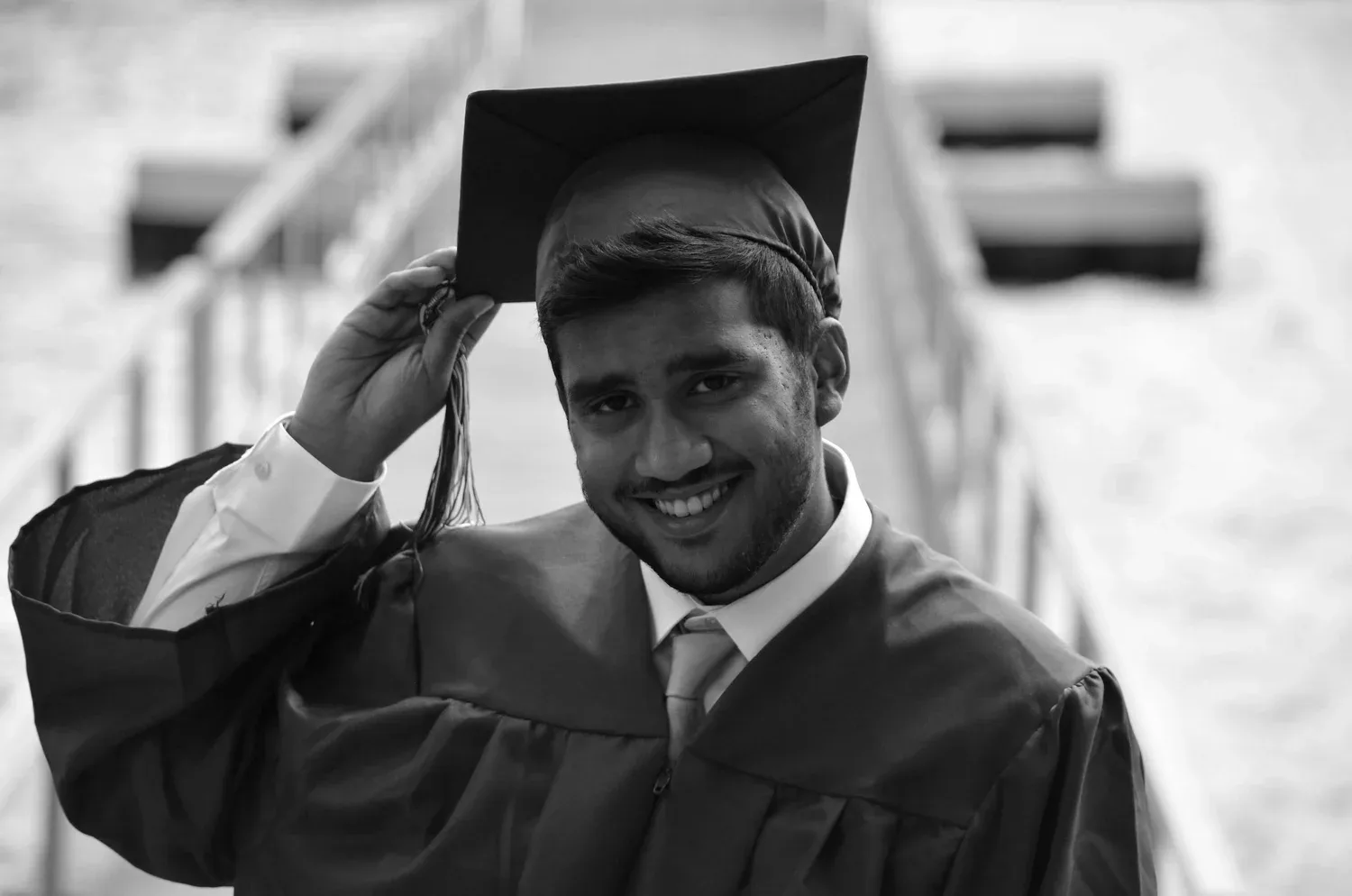 Black-and-white photo of a smiling graduate adjusting his cap