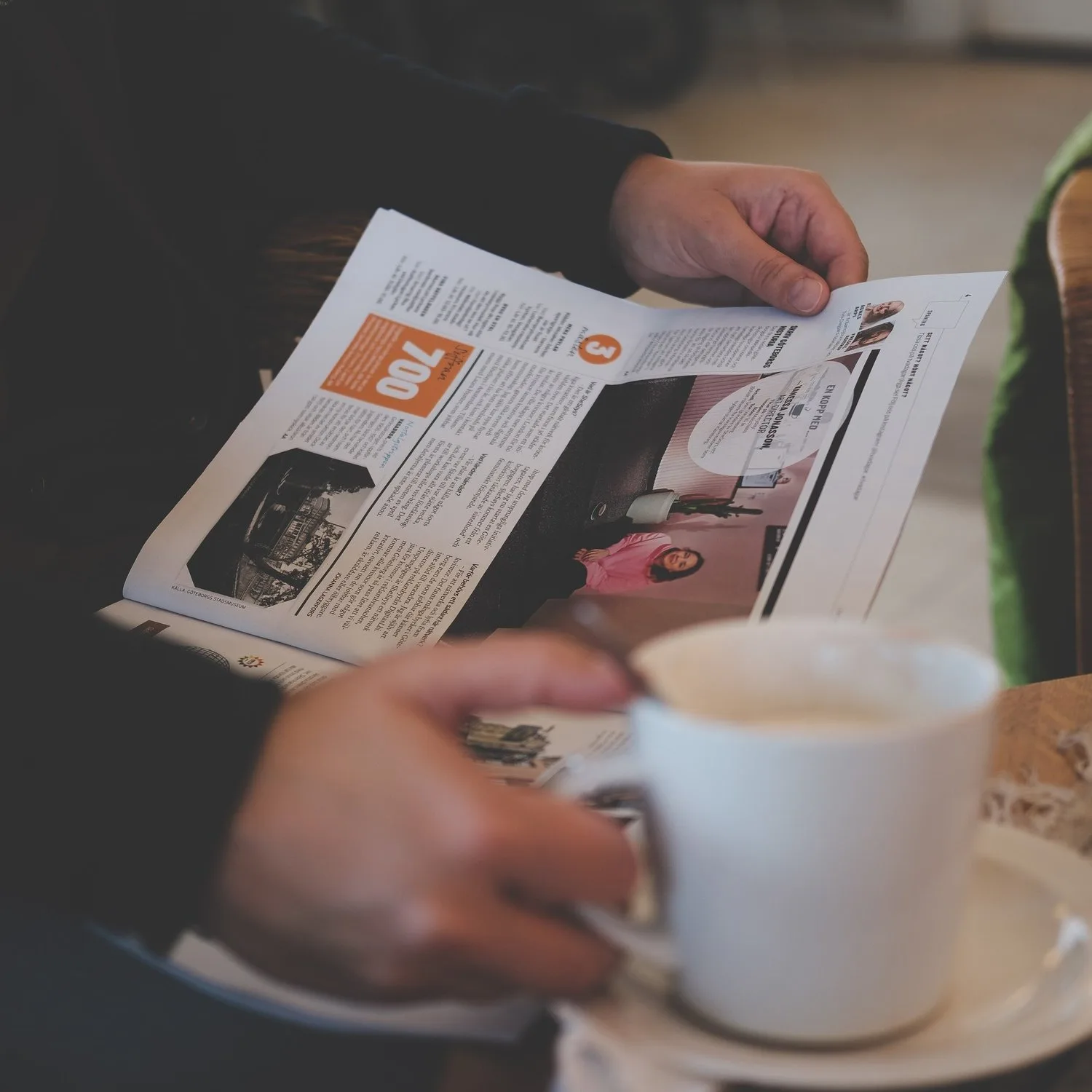 Hands holding a newspaper and a cup of coffee