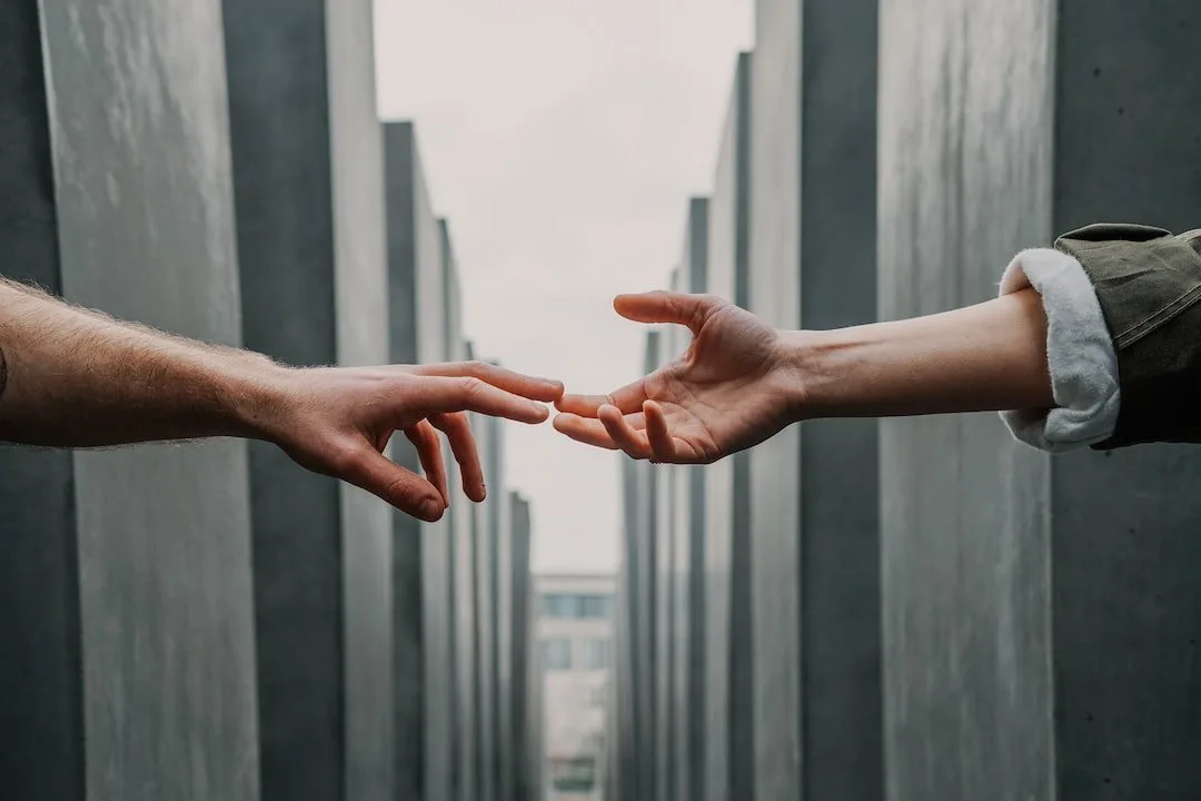 Two hands reaching toward each other between tall concrete walls