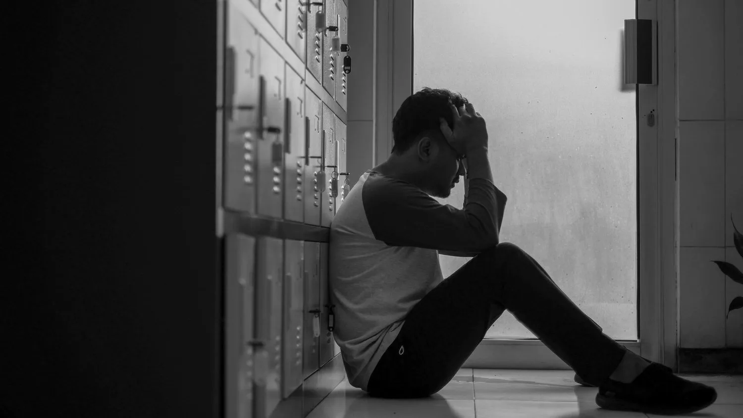 Black-and-white photo of a person sitting on the floor with their head down