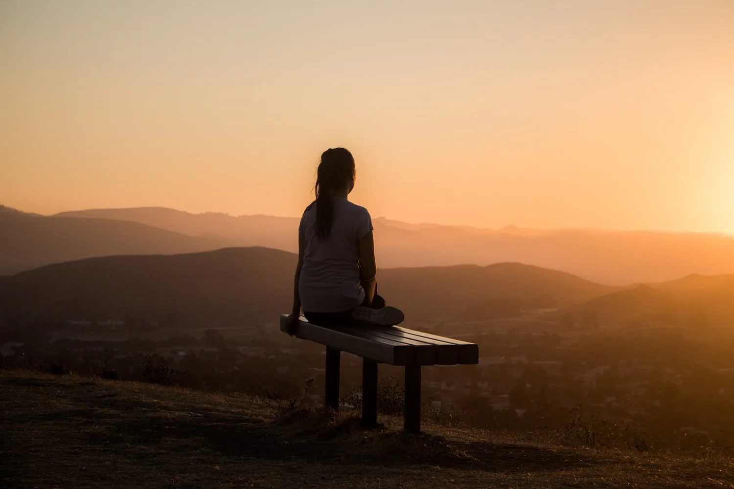 Person sitting on a bench on a hilltop at sunset