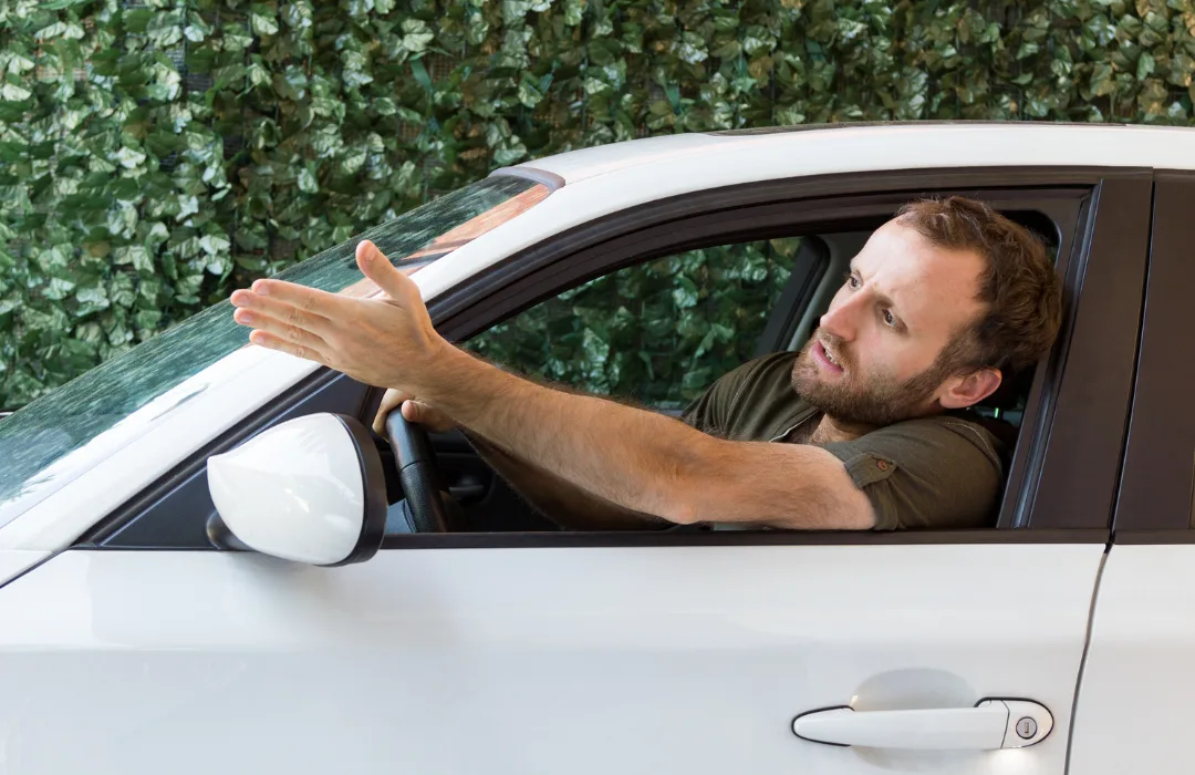 Frustrated man gesturing out the window of a white car